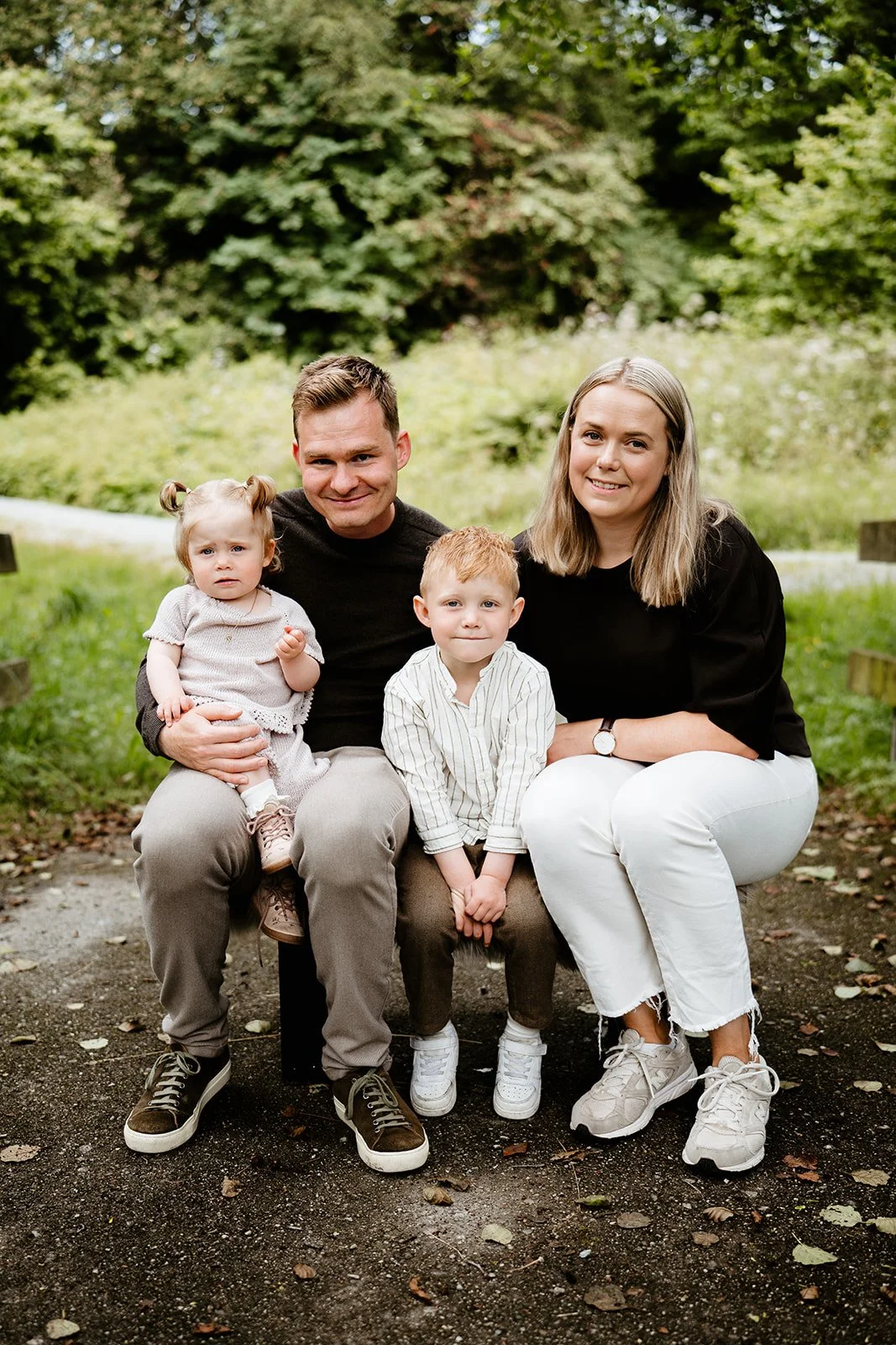 Familieportrett av foreldre med en liten datter og sønn utendørs i en grønn park