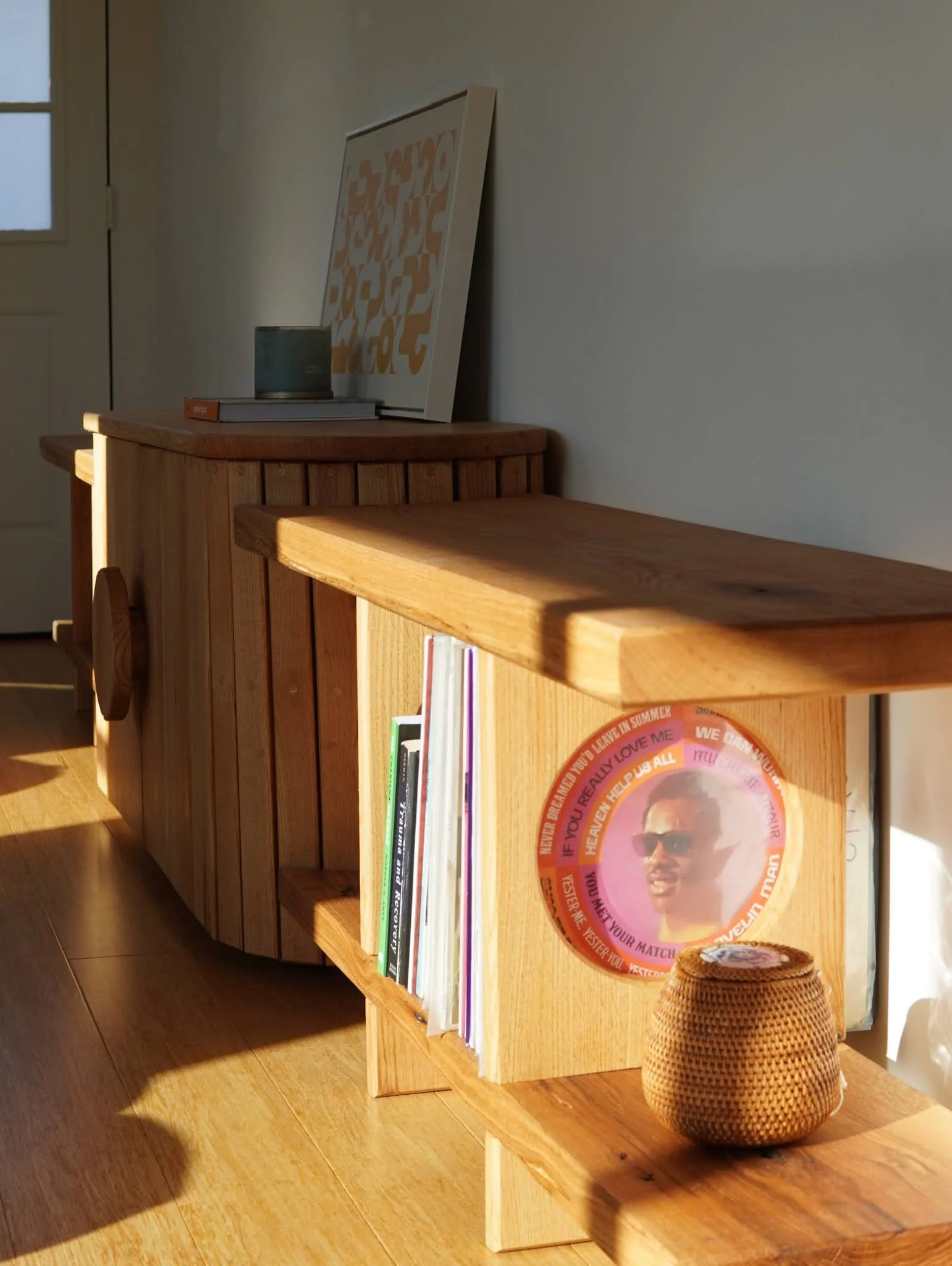 A custom wooden bookshelf with books, framed artwork, and decorative items in sunlight.