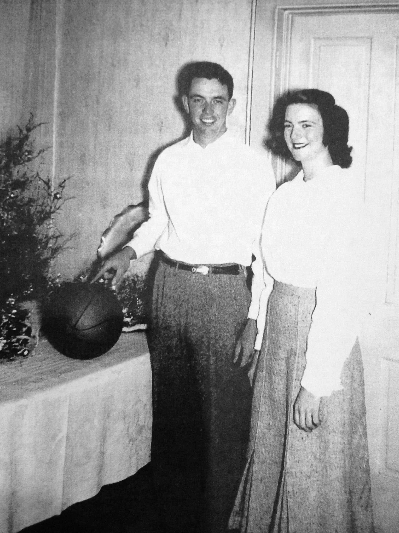 A black and white photo of a couple standing indoors, smiling at the camera.
