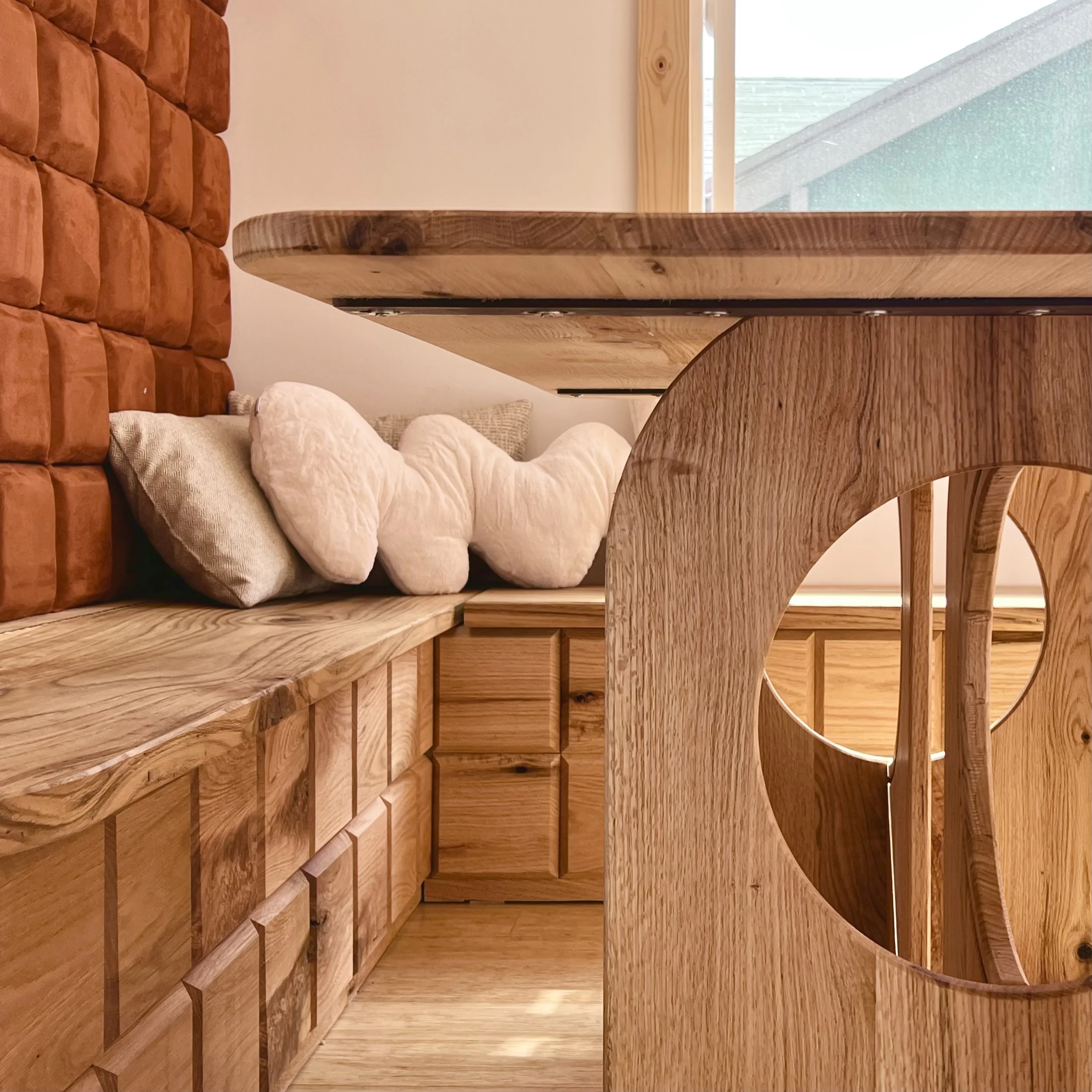 Close-up view of a wooden dining table and chair with a cutout circle design, and decorative pillows in the background.
