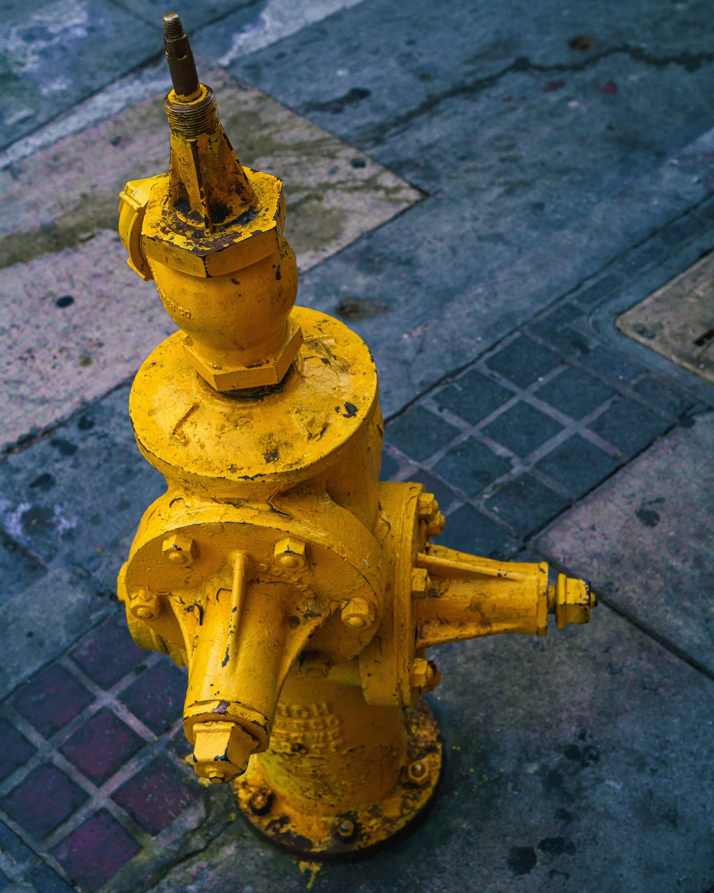 A bright yellow fire hyrdrant on a dark blue asphalt and brick street corner