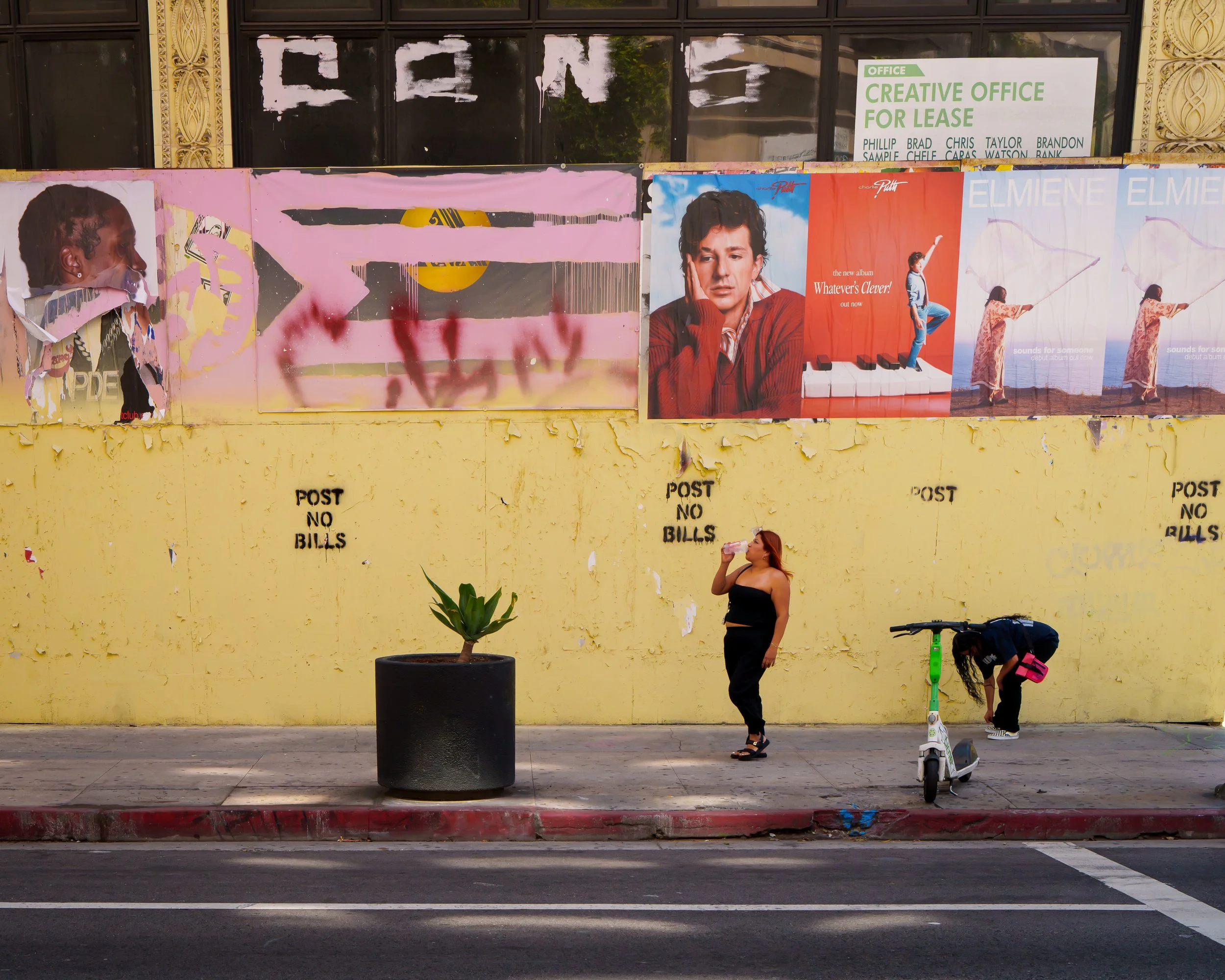 Two women enjoying Sunday afternoon in downtown Los Angeles in front of a wall full of poster and printed Post No Bills