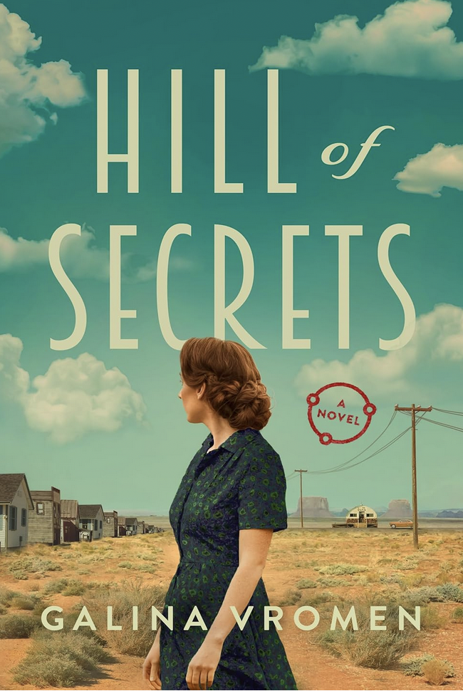 Book cover for 'Hill of Secrets' by Galina Vromen showing a woman with red hair in a blue dress standing in a desert landscape with houses, power lines, and a bus in the background, under a partly cloudy sky.