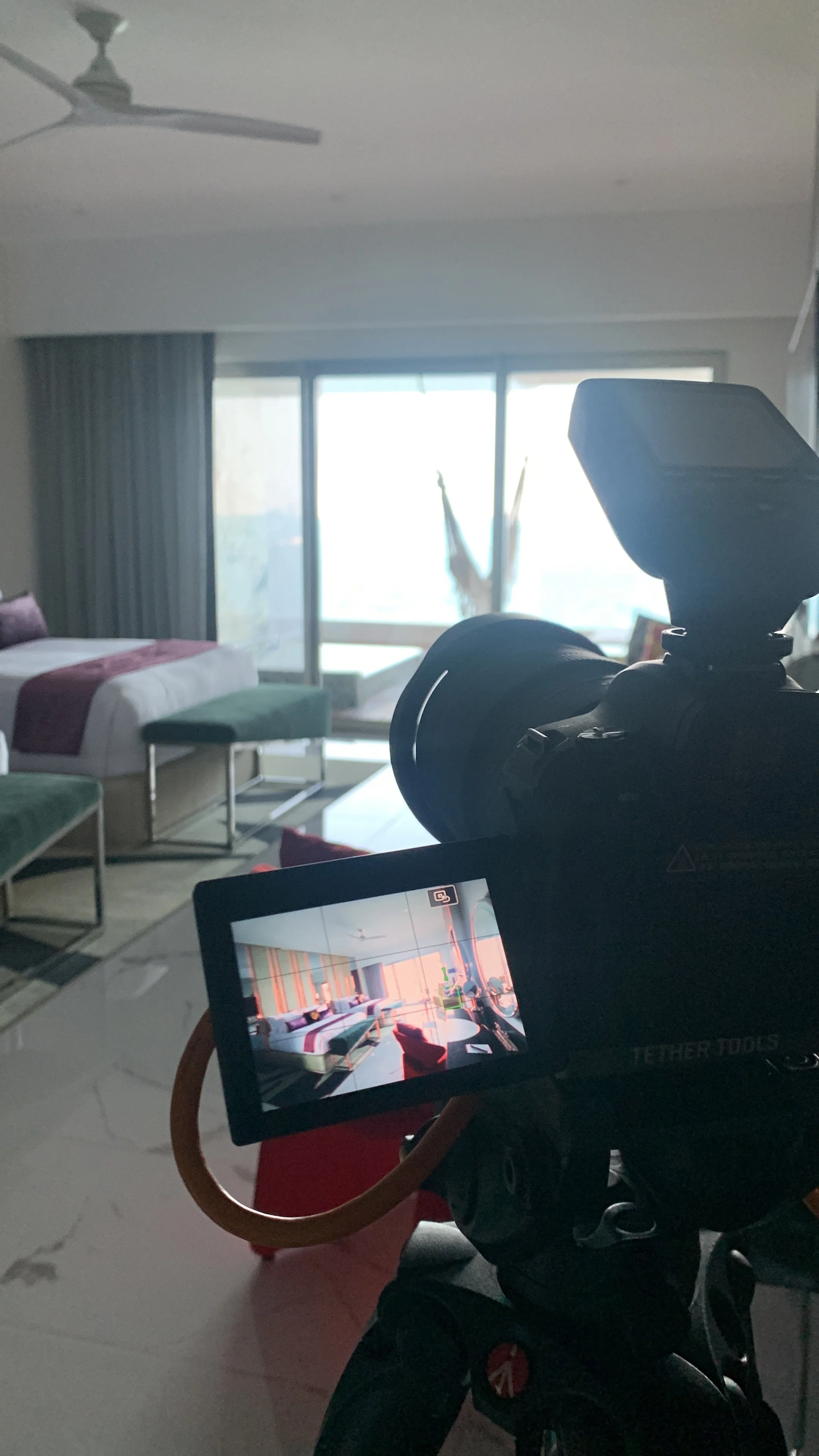 Camera recording a hotel room with bed, chairs, and large window, capturing interior decor and furniture.