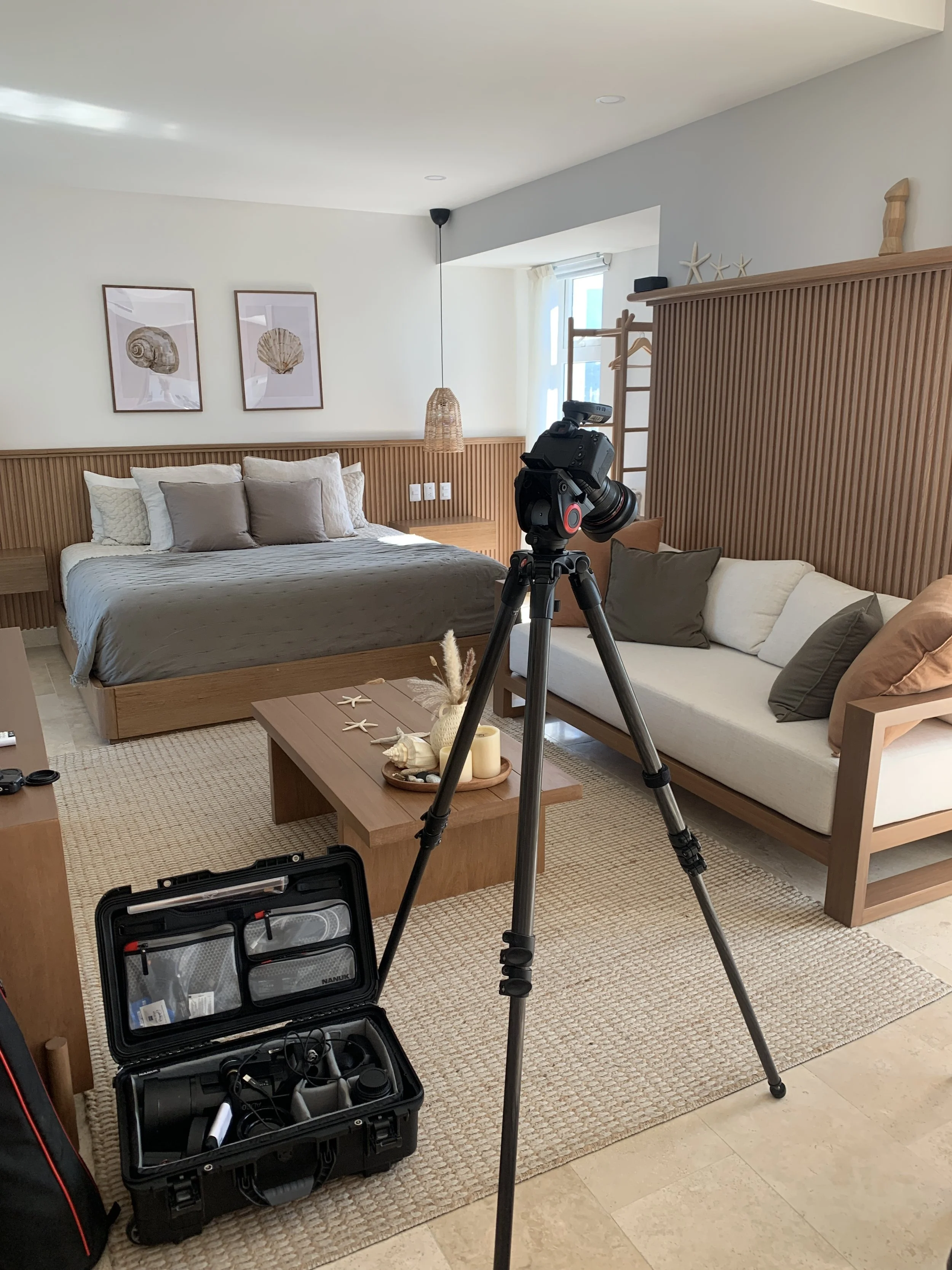 A hotel or resort room with a bed, couch, coffee table, and camera equipment set up for filming or photography in a beach-themed decor.