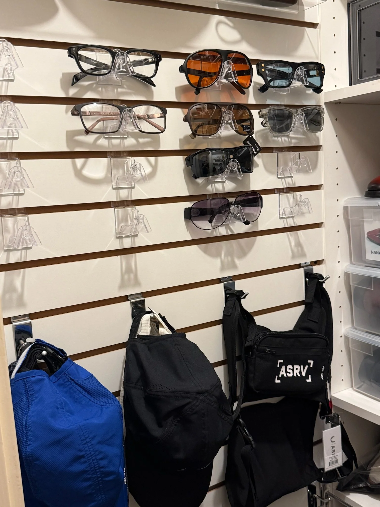 Display of various sunglasses on clear stands, with bags hanging below, in a retail store.