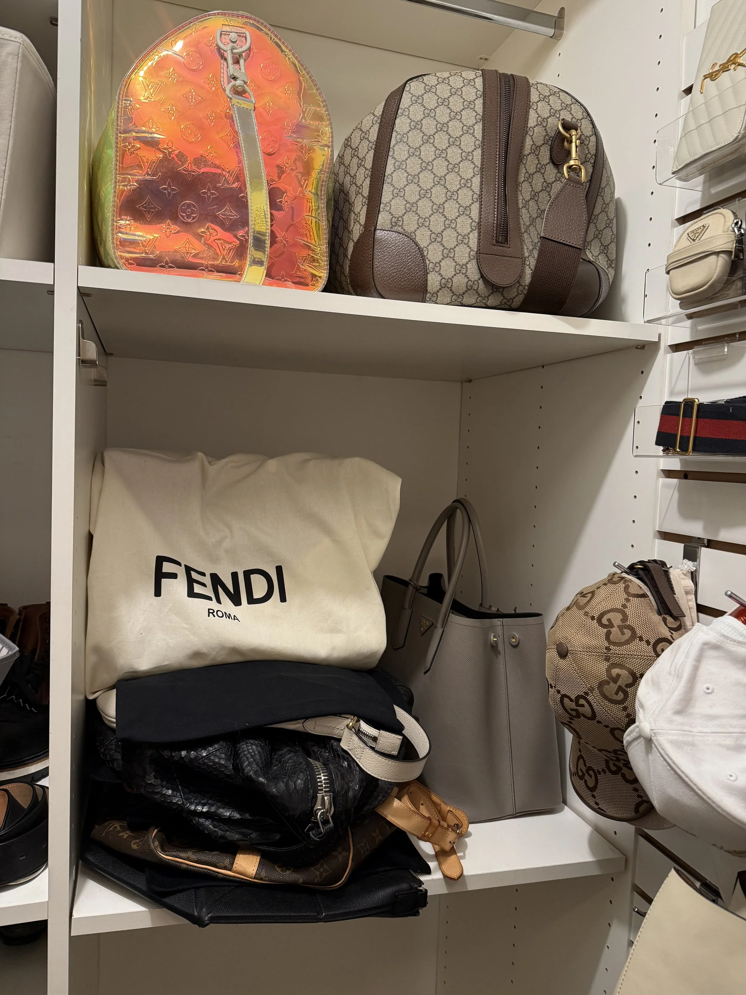 Shelf with designer bags, including a Louis Vuitton bag, a Gucci GG Supreme fabric bag, and a Fendi Roma tote, among other accessories and footwear.