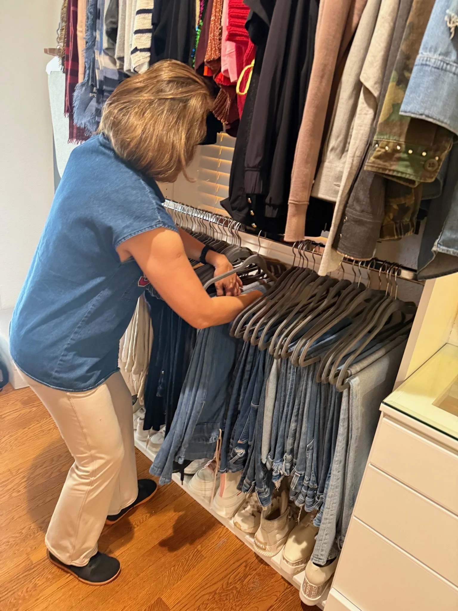 A woman shopping for clothes in a retail store, browsing a rack filled with various garments including jeans, sweaters, and jackets.