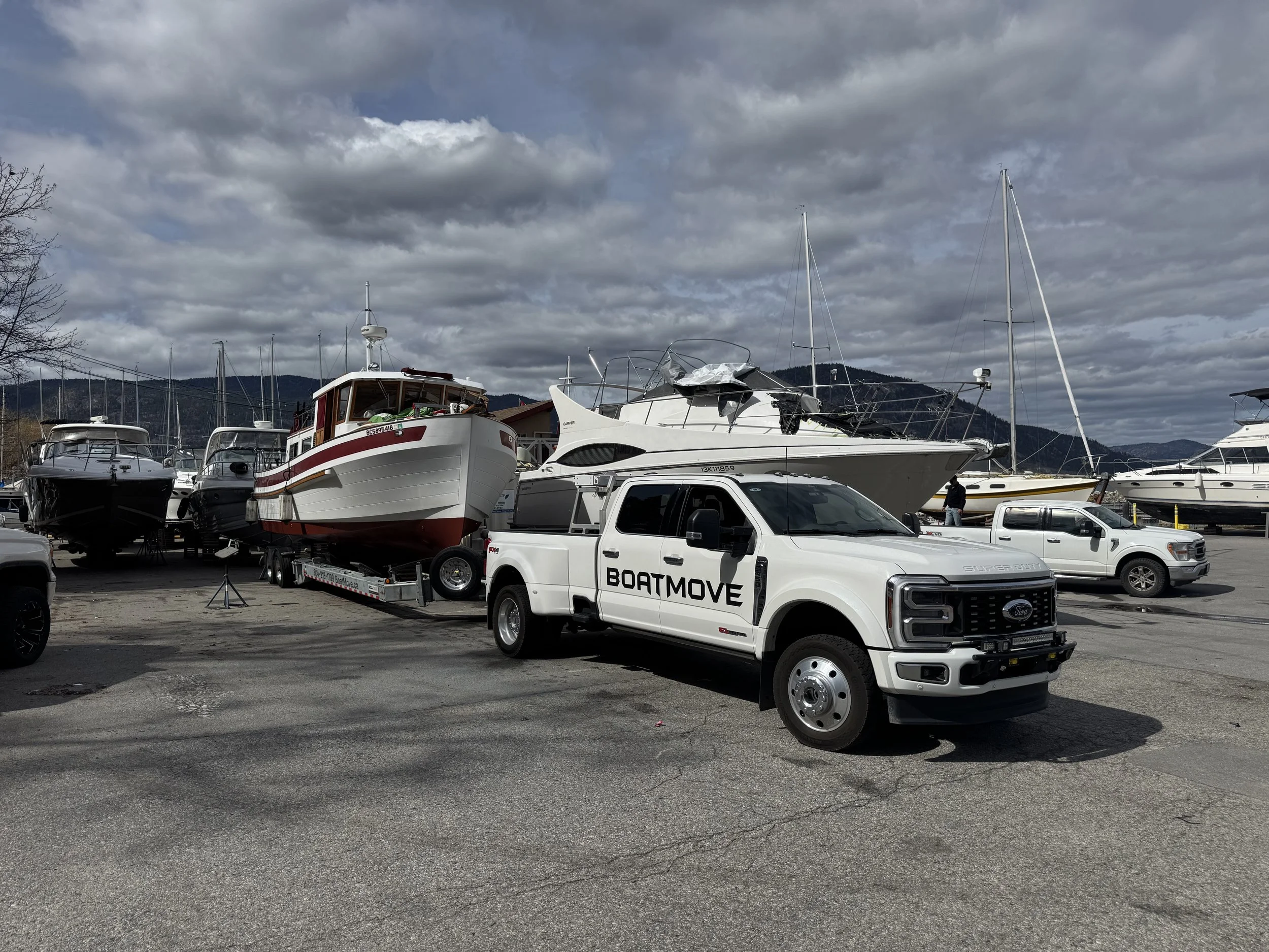 Marina parking lot with boats on trailers and parked trucks under a cloudy sky.