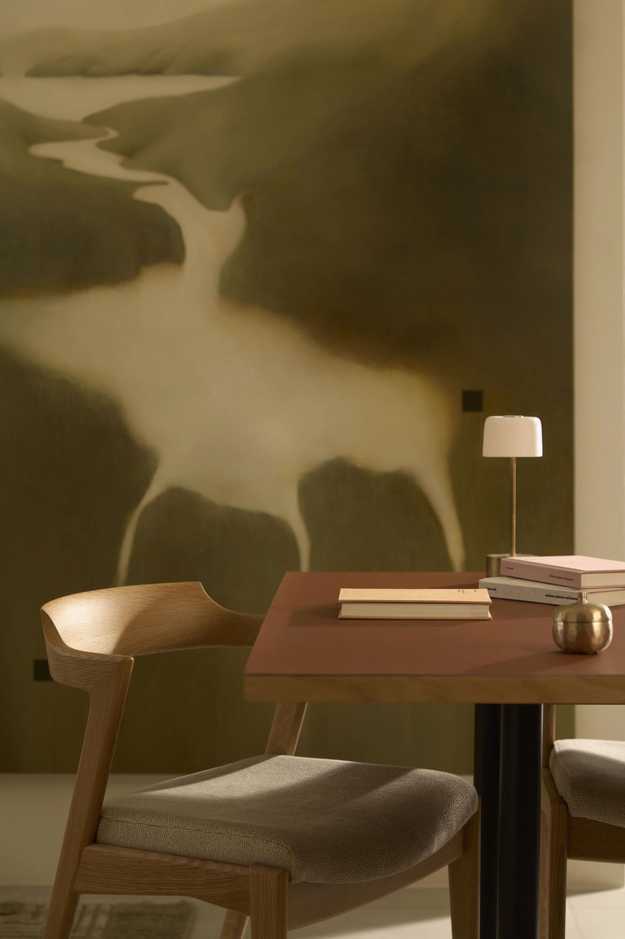 Interior of a room with a wooden table, a wooden chair with a cushioned seat, a table lamp, and a large abstract painting on the wall.