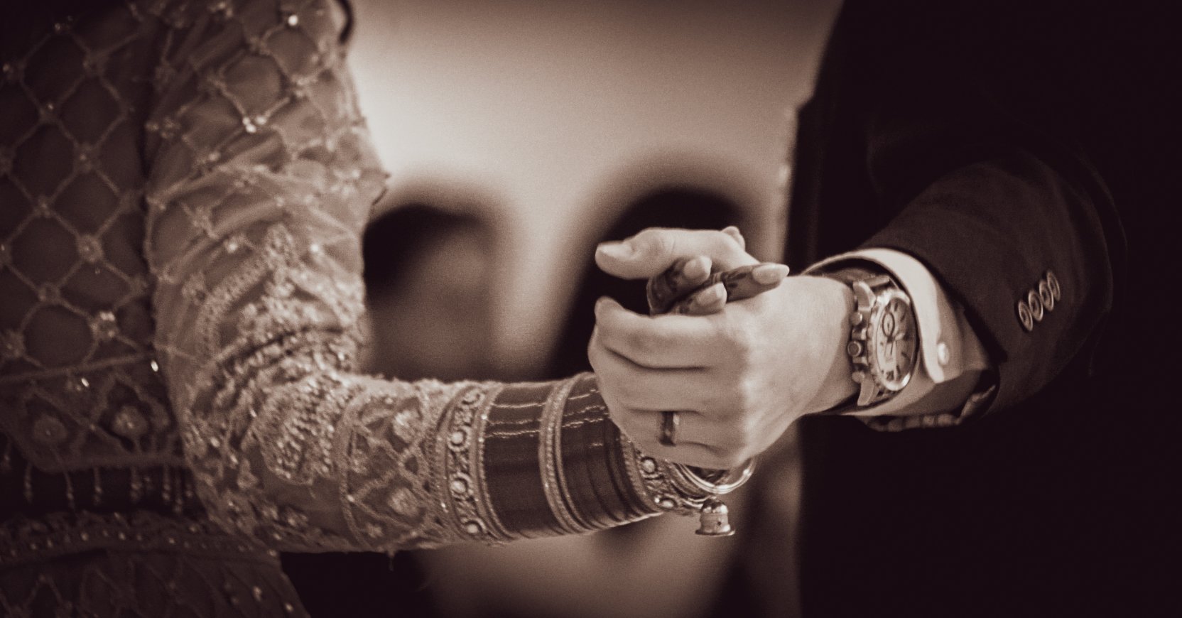 Close-up of two people dancing holding hands, one wearing a detailed patterned sleeve and the other wearing a suit with a watch.