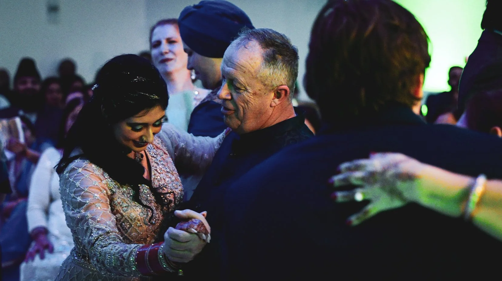People dancing together at a celebration or wedding, with a woman in traditional attire and a man smiling while dancing.