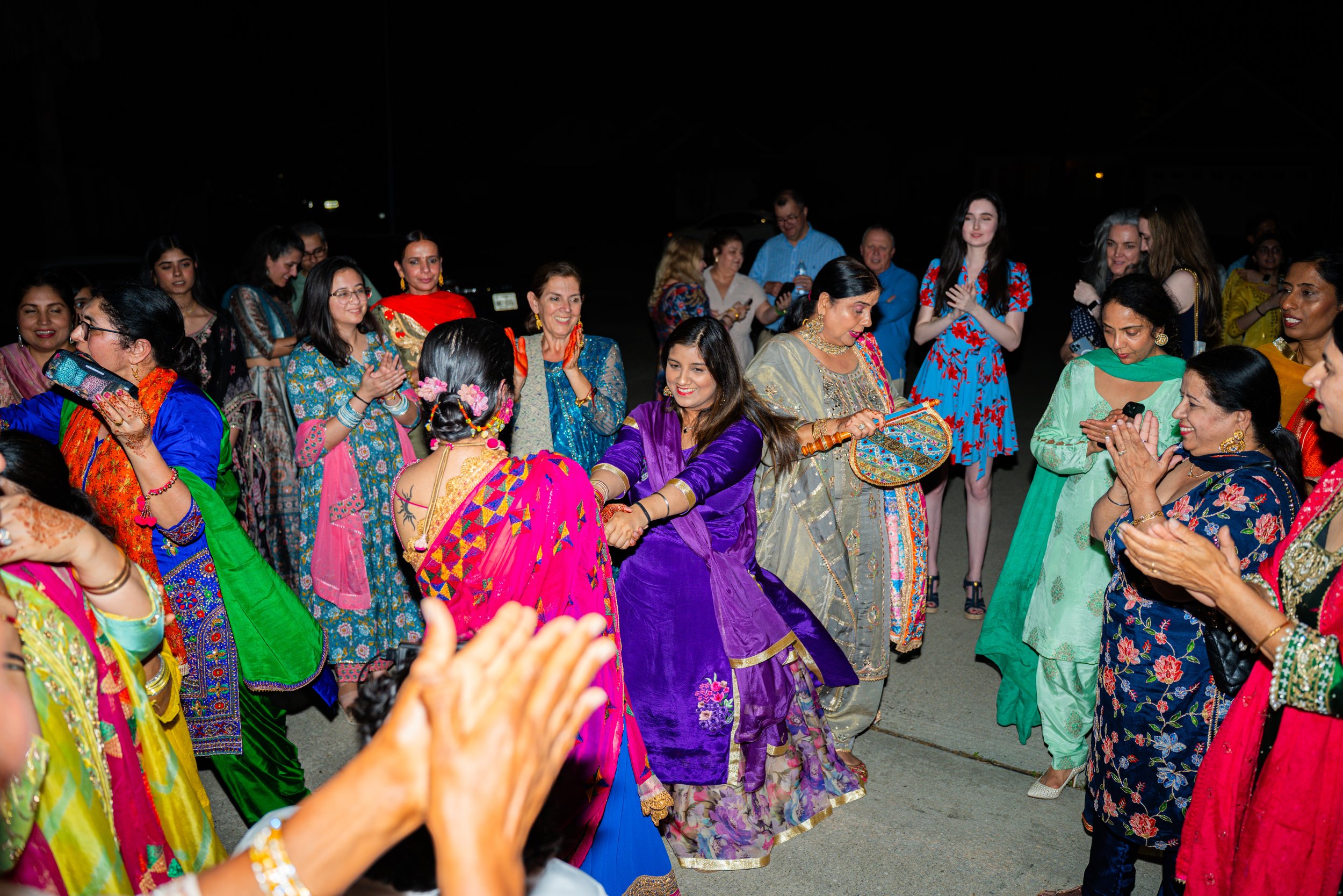 Group of women dressed in colorful traditional Indian clothing dancing and celebrating together outdoors at night.