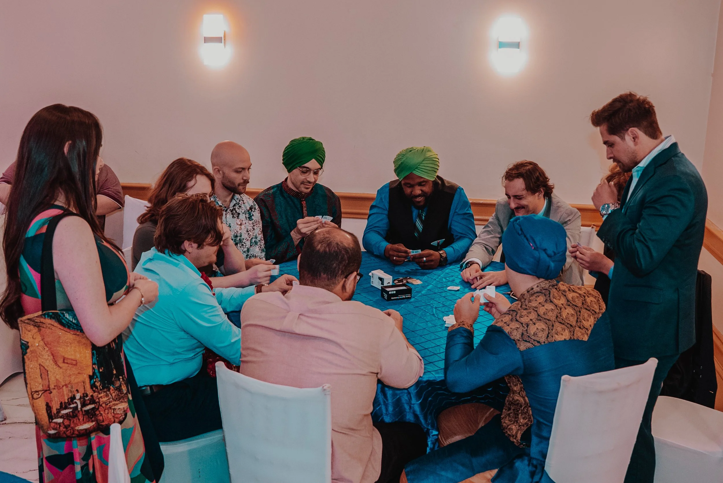 People playing a card game around a table in a room with wall sconces.