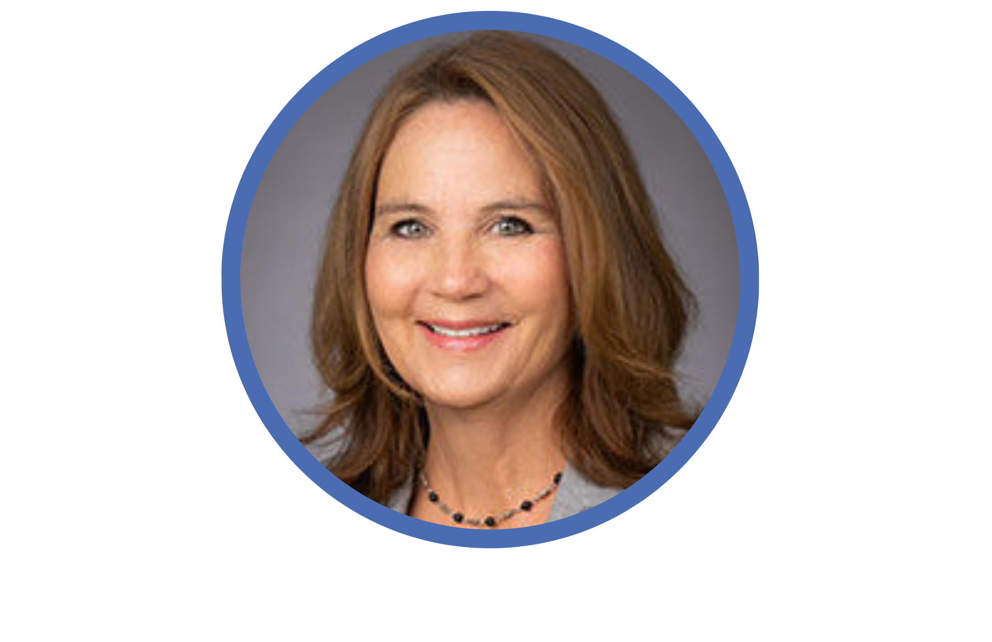 Headshot of a smiling woman with shoulder-length brown hair wearing a gray blazer and a black beaded necklace.
