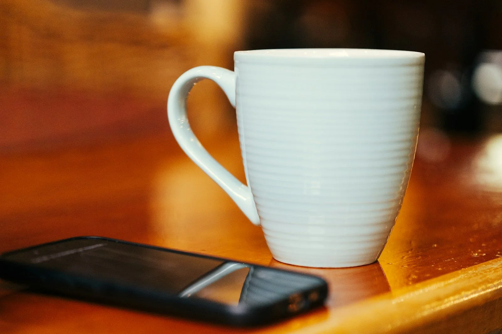 A white mug beside a phone lying face down on a wooden table