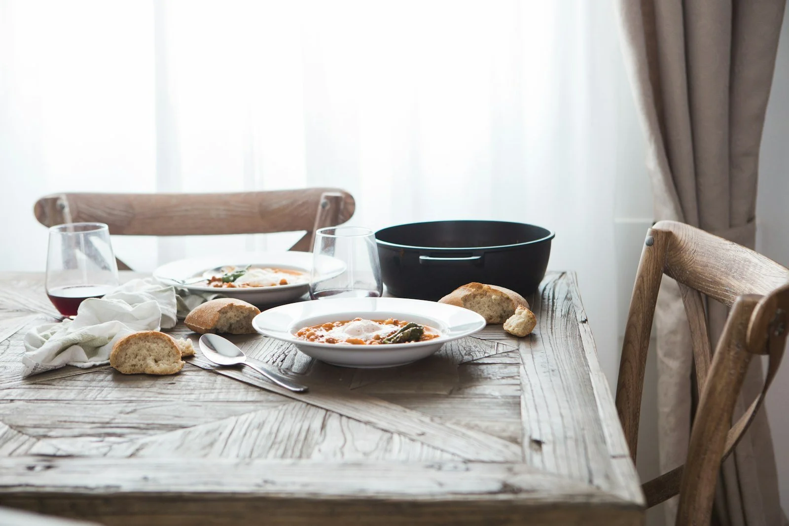 A table set for two by a window, with bowls, bread, and glasses