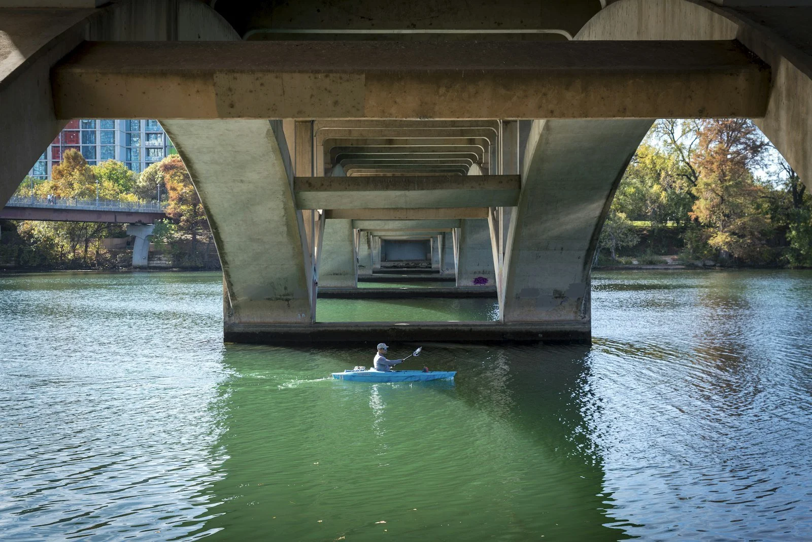 A kayaker on Lady Bird Lake, under a bridge in Austin