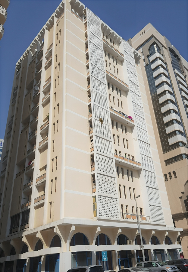 A tall beige apartment building with balconies and decorative white lattice panels, set against a clear blue sky.