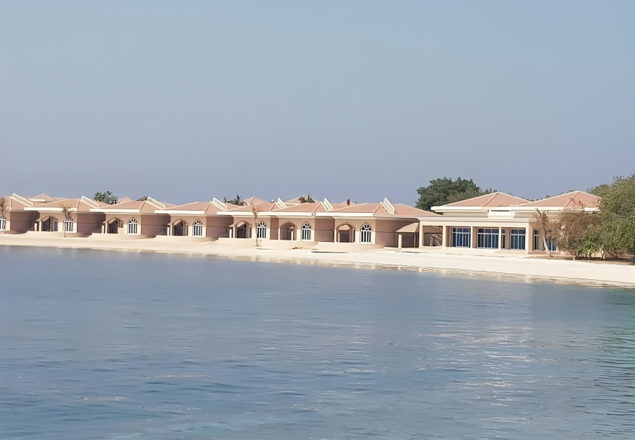 Waterfront resort buildings with arches and beige facades, clear blue sky, and calm water.