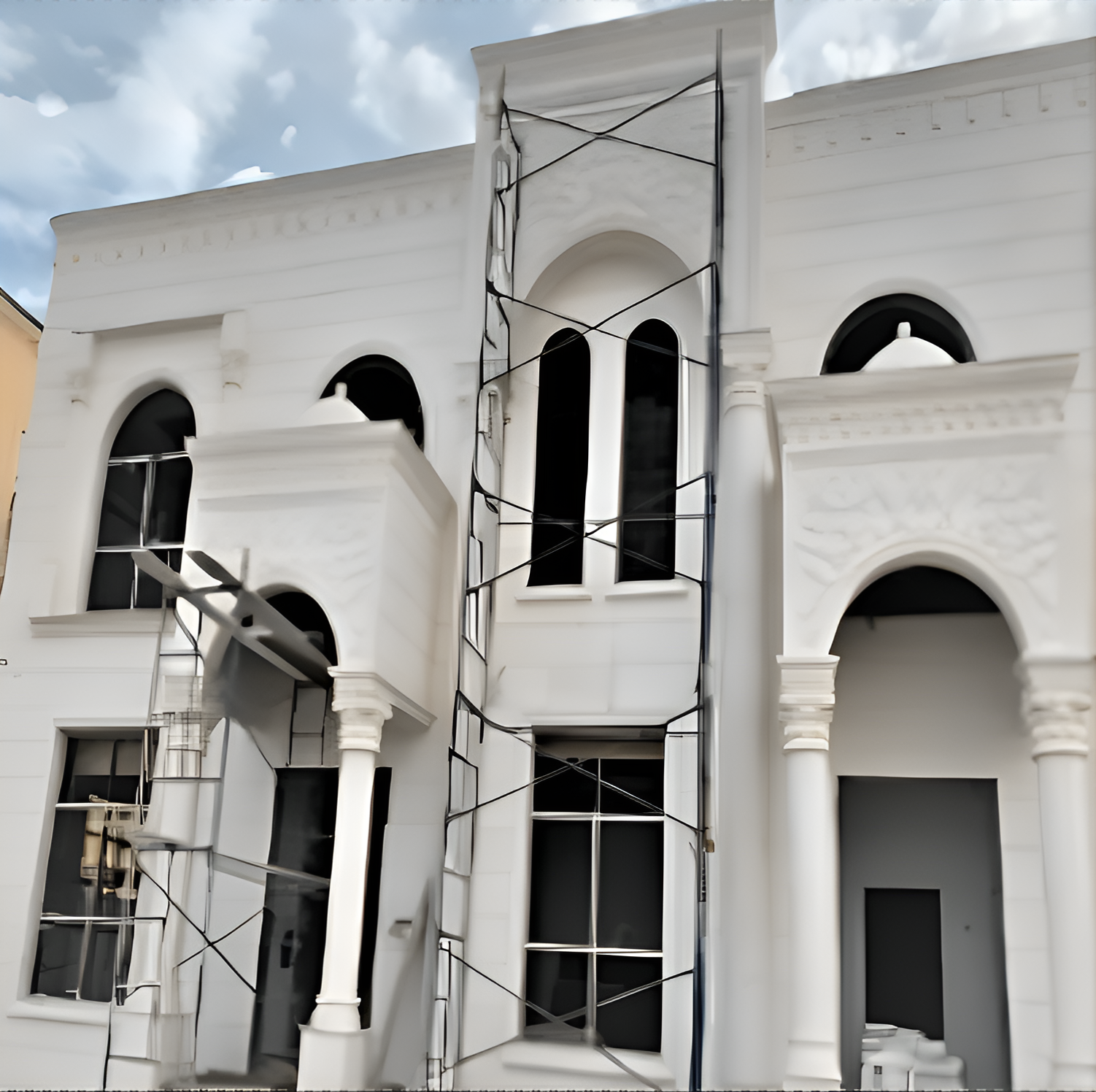 White building under construction with scaffolding and tall arched windows.