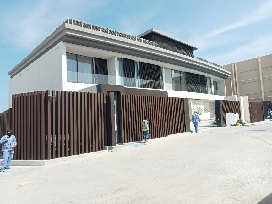 Large modern house with glass windows and wooden fence, people in work uniforms nearby