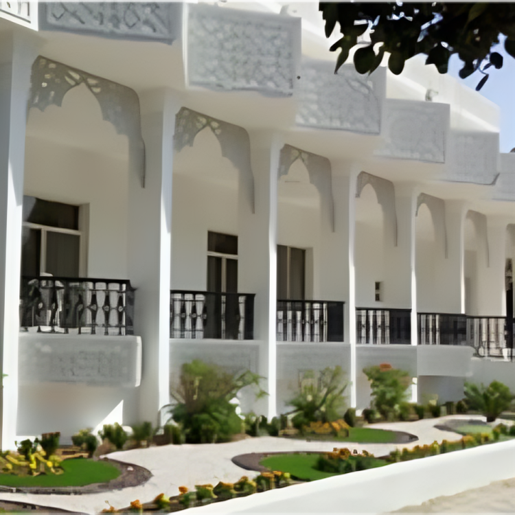 Traditional Middle Eastern architecture with white walls, arched windows, and ornate balcony railings. A garden with bushes and flowering plants is in the foreground.