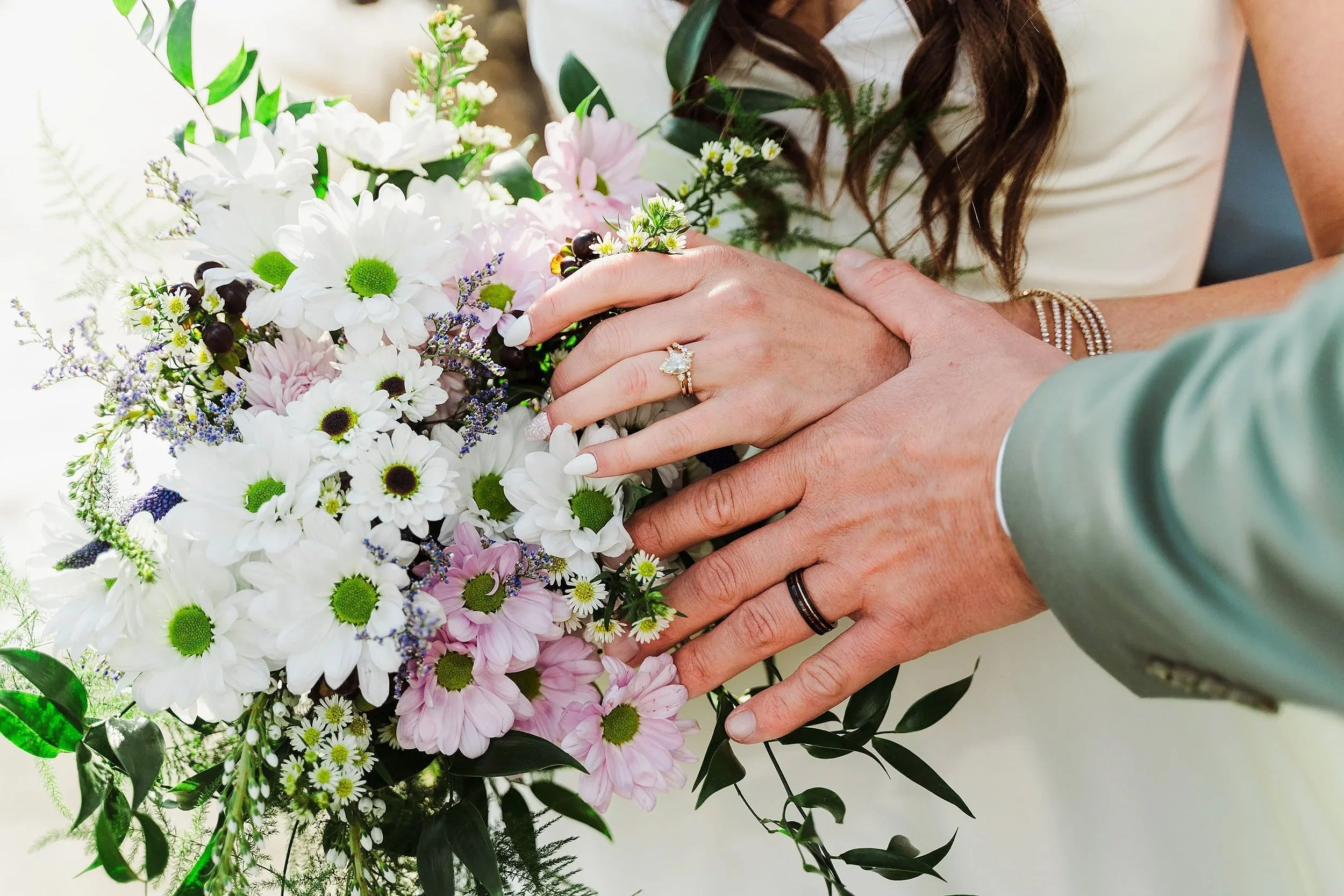 Close-up of a couple holding hands over a colorful bouquet of flowers, with the woman wearing a ring, at a wedding or romantic event.