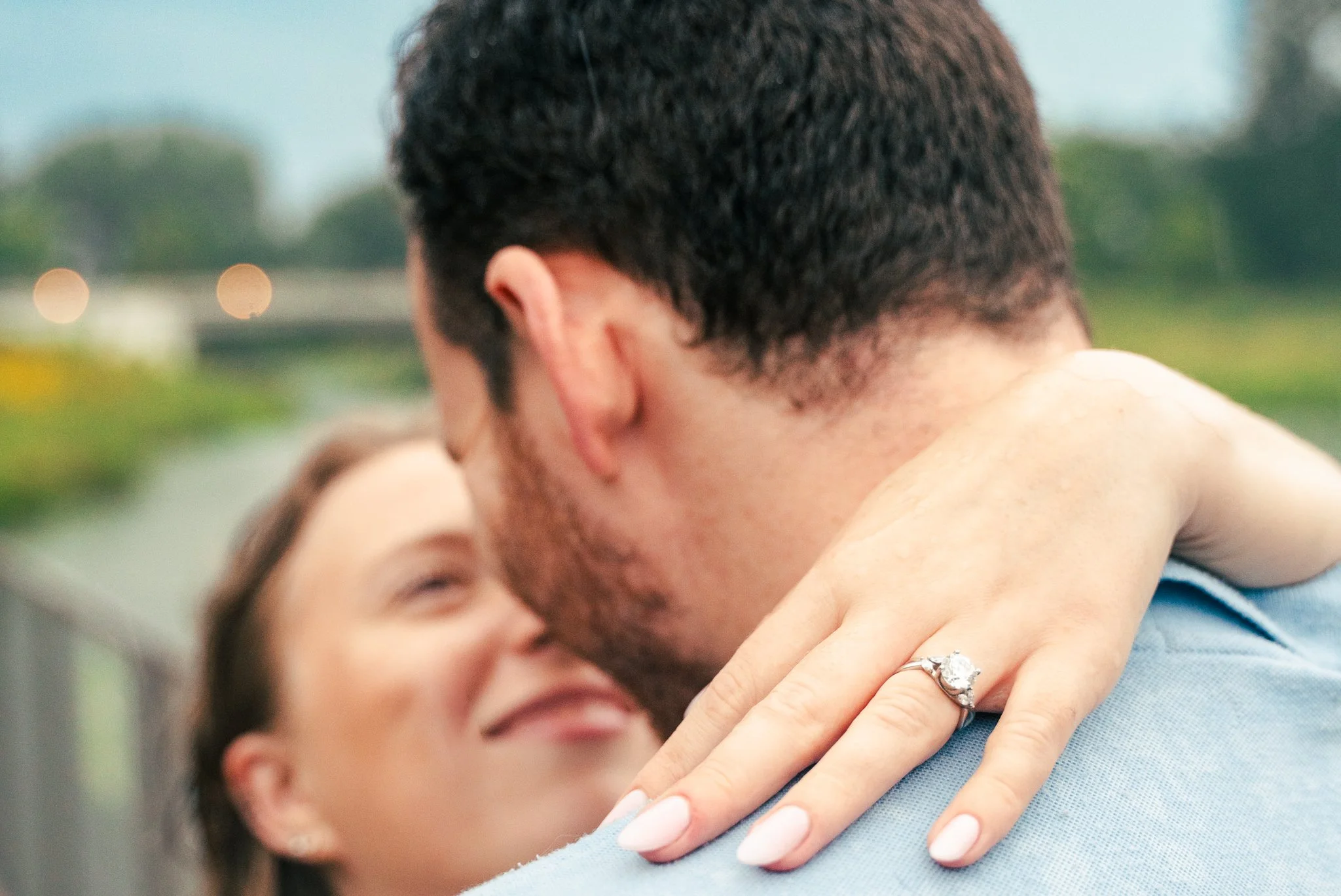 Lincoln Park Chicago Illinois Engagement Photographer | Shot from over grooms shoulder, bride puts hand with engagement ring on his shoulder, bride looks at groom in background | Midwest Wedding and Engagement Photography Sessions