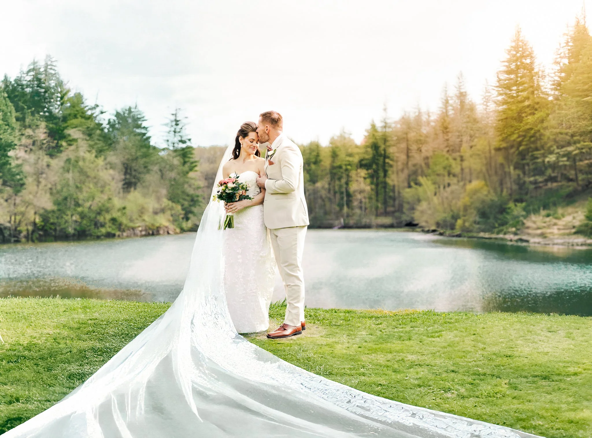 A bride and groom embrace outdoors near a lake with a forested background during their wedding.