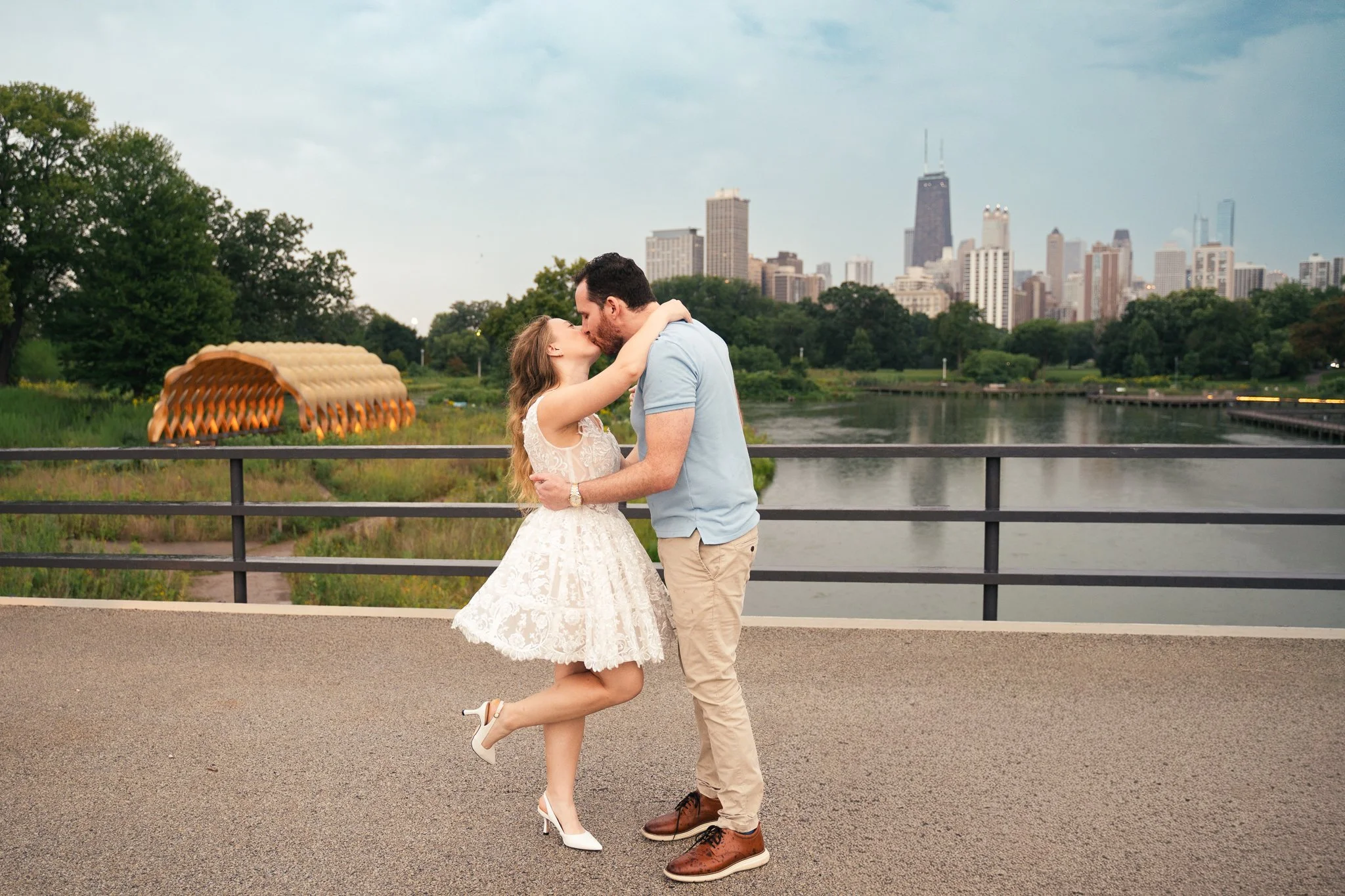 Lincoln Park Chicago Illinois Engagement Photographer | Bride in lace white dress kissing groom with leg popping in air, Honeycomb in background | Midwest Wedding and Engagement Photography Sessions