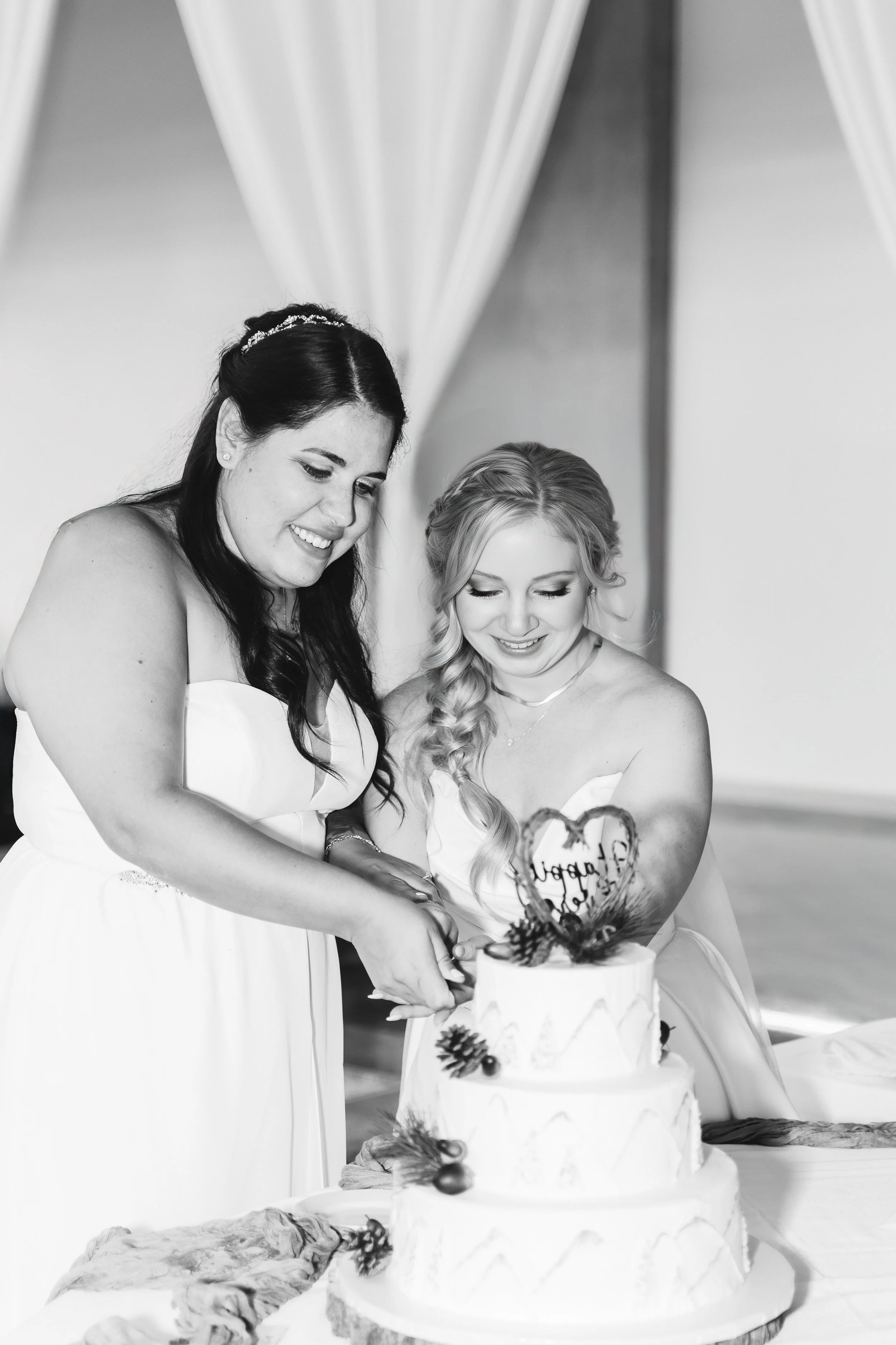 Two women in wedding dresses cutting a wedding cake together at a celebration.