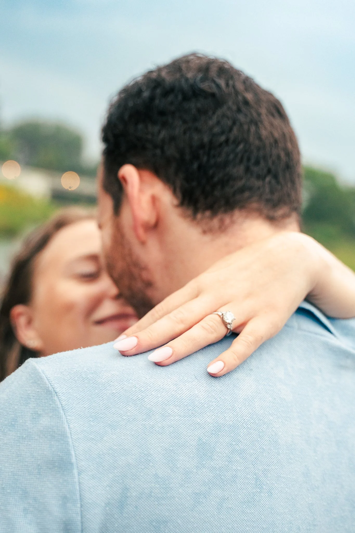 Lincoln Park Chicago Illinois Engagement Photographer | Shot from over grooms shoulder, bride puts hand with engagement ring on his shoulder, bride looks at groom in background | Midwest Wedding and Engagement Photography Sessions