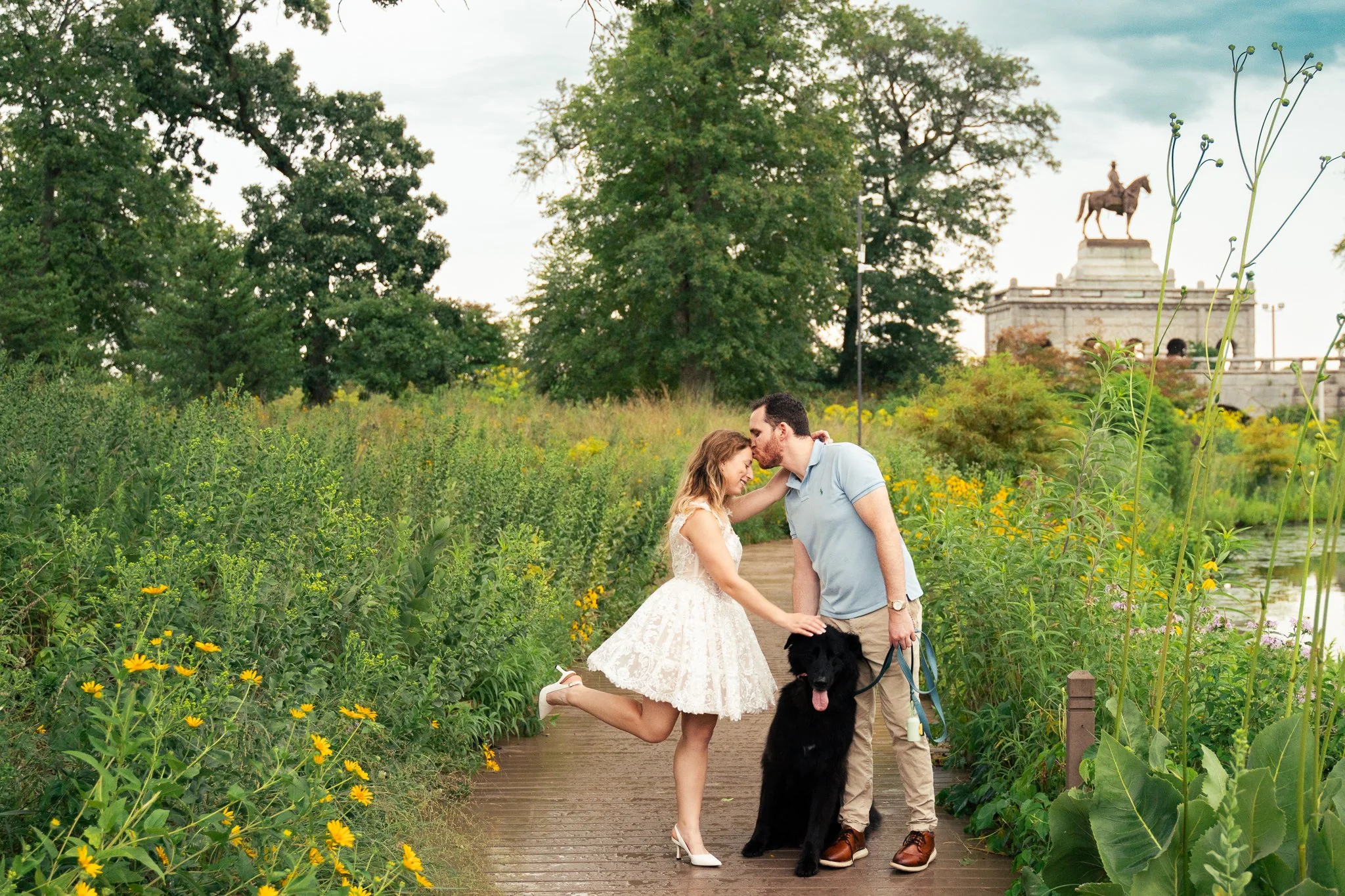 Lincoln Park Chicago Illinois Engagement Photographer | Bride in lace white dress popping up leg, groom kisses her on the forehead, black pet dog between them | Midwest Wedding and Engagement Photography Sessions