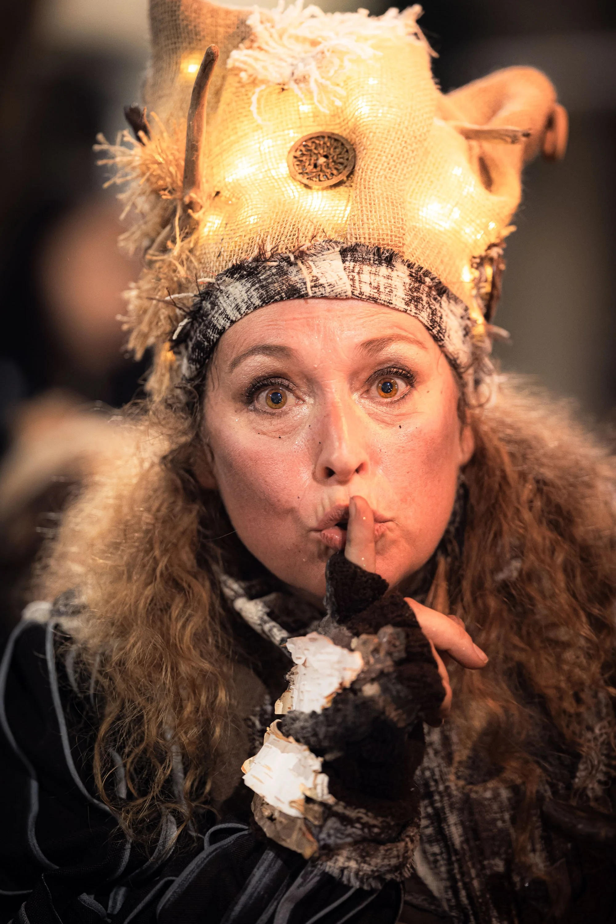 Personne avec un chapeau décoratif illuminé, faisant un geste de silence, doigt sur les lèvres.
