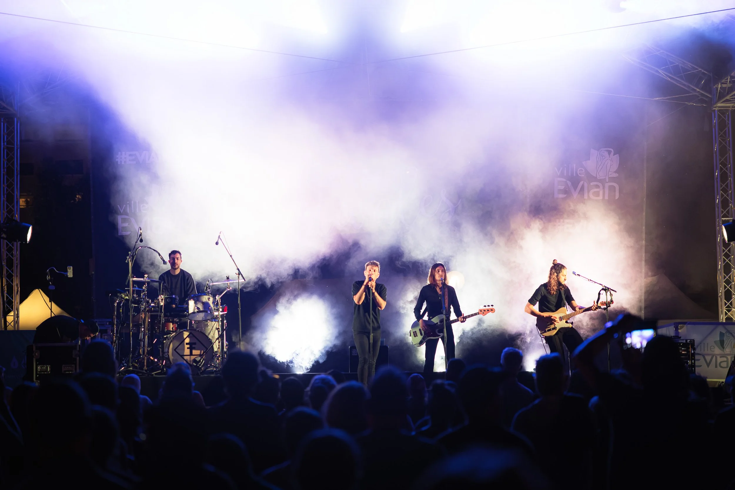 Groupe de musique en concert sur scène avec éclairage lumineux et fumée.