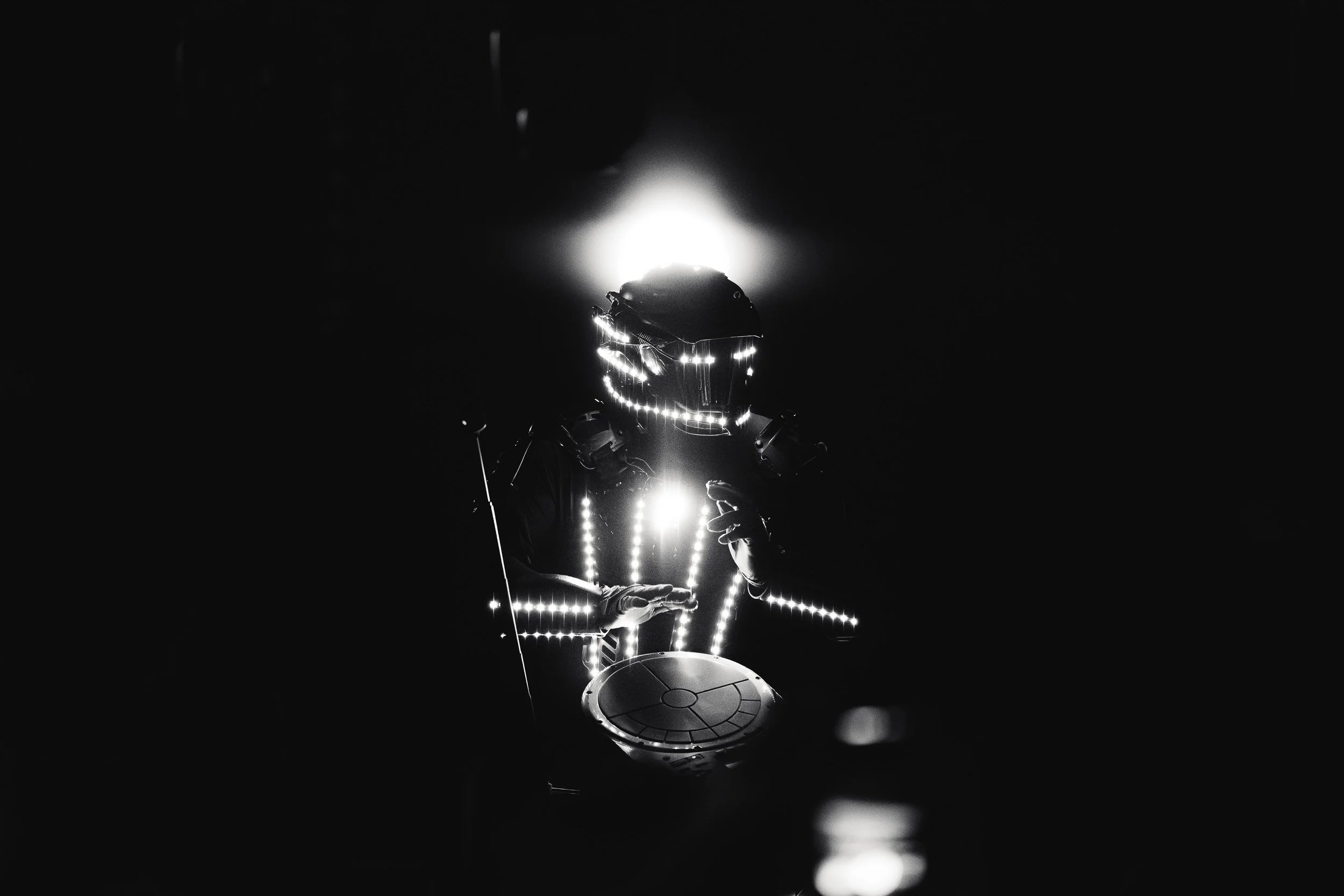 Une personne portant un casque de réalité virtuelle avec des lumières LED, jouant d'un instrument électronique dans un environnement sombre.