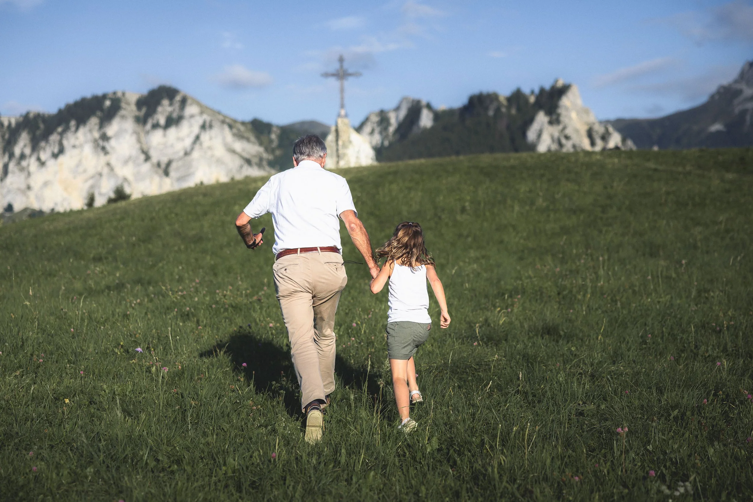 Photo de famille en Haute-Savoie par le photographe Rüdi Welter. Une petite fille et son grand père qui courent vers une croix en montagne.