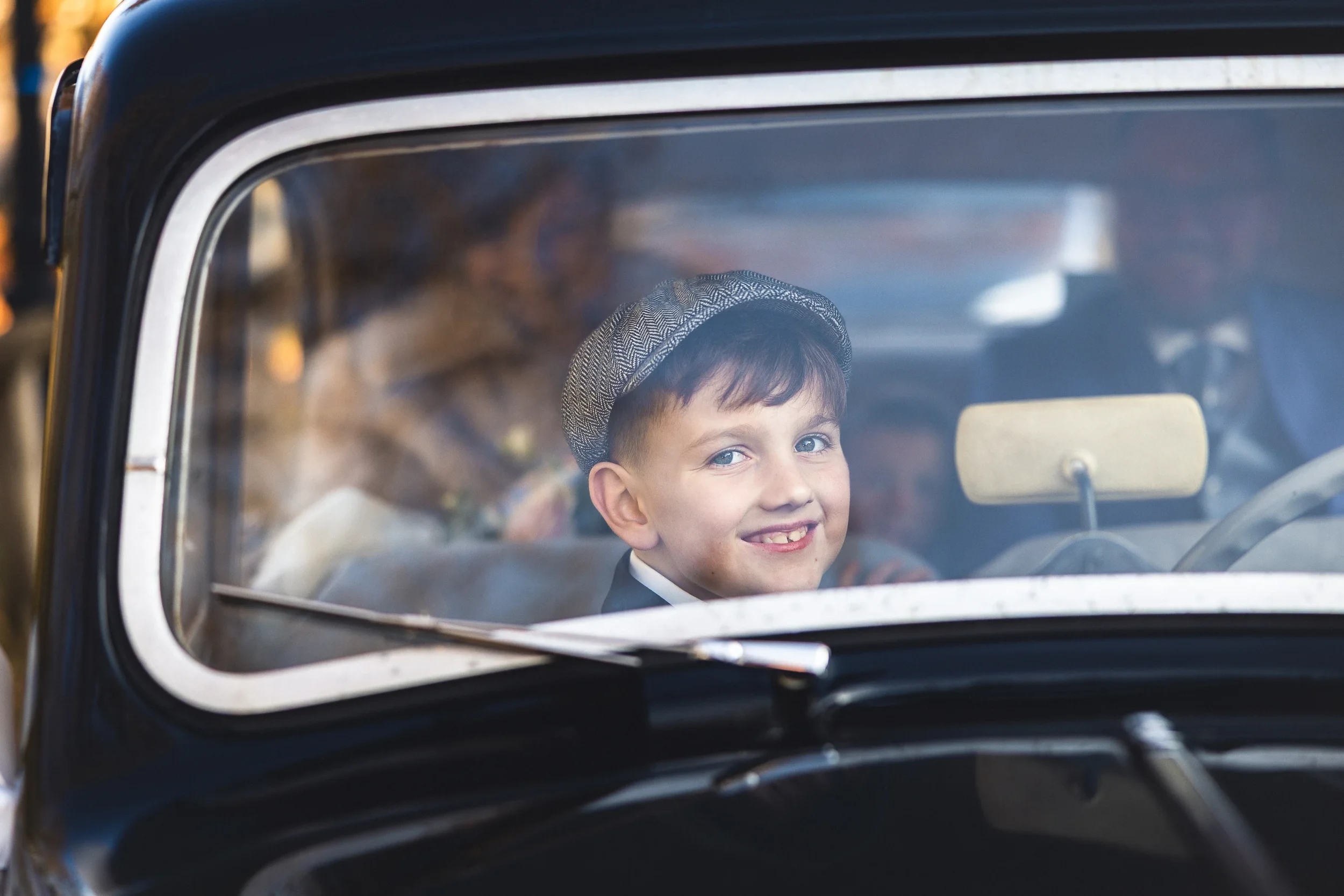 Enfant des mariés avec un chapeau qui regarde à travers la vitre d'une voiture.