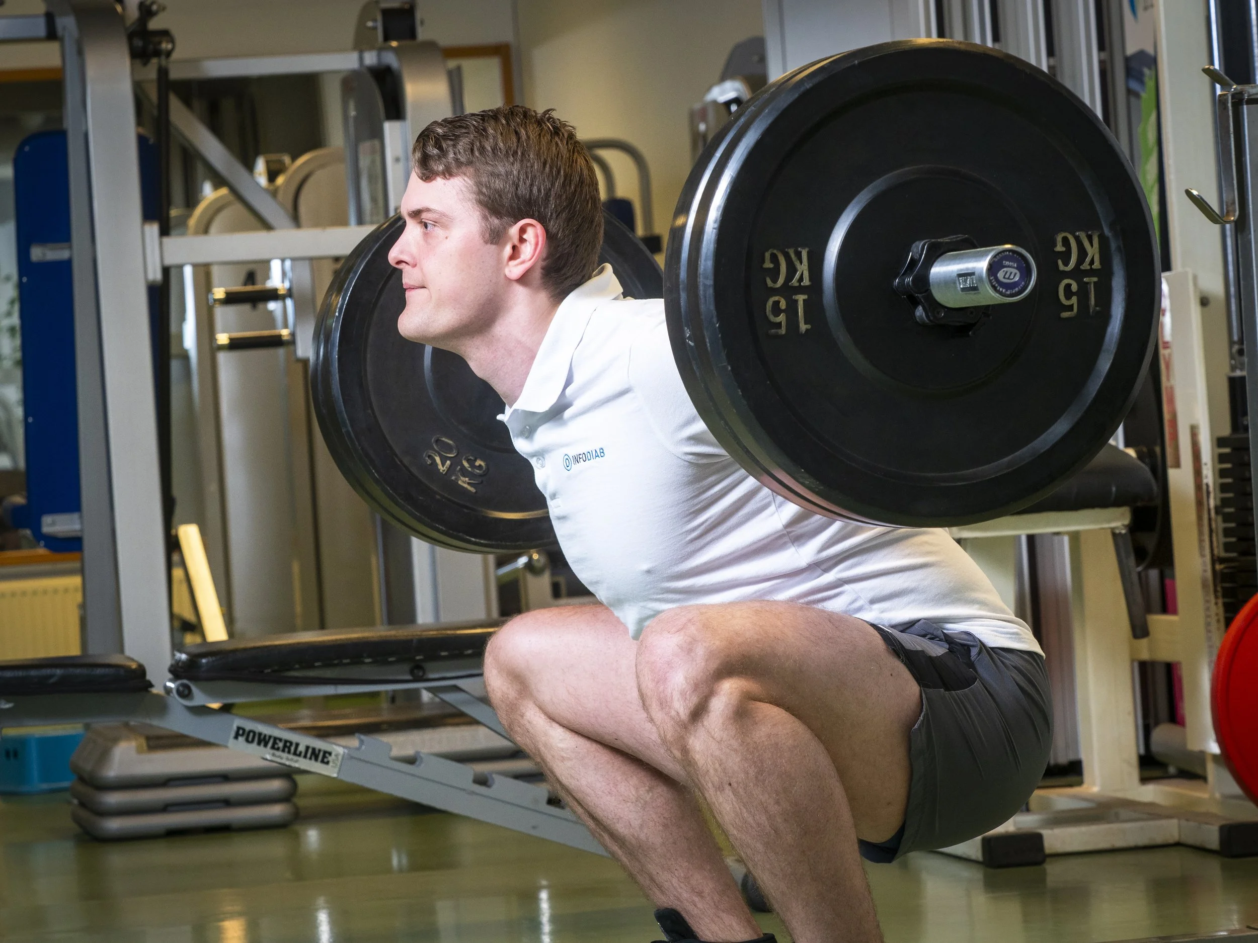 Man som gör en squat med vikt på ryggen i ett gymmiljö.