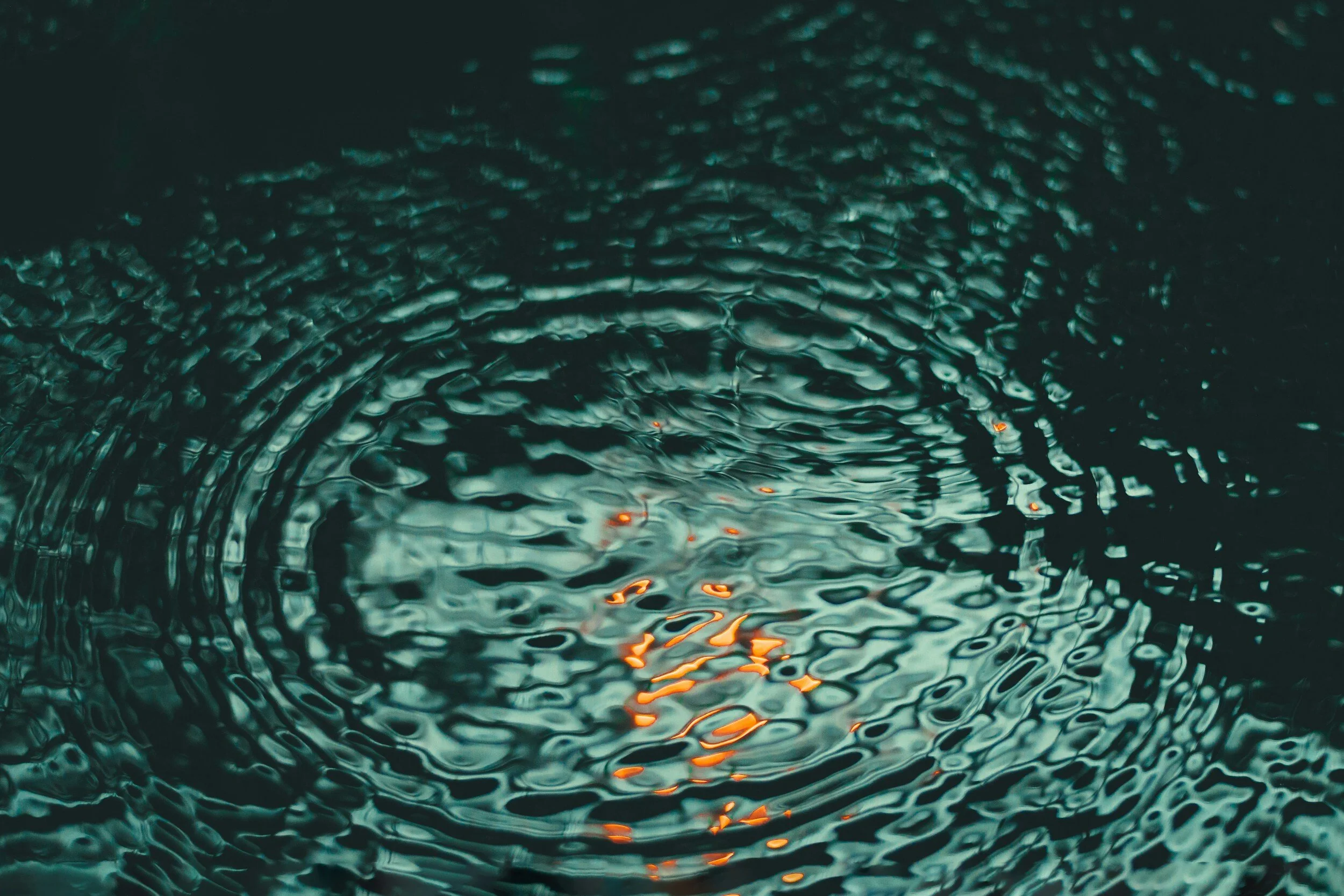 Close-up view of dark, rippling water surface with reflections of orange lights.
