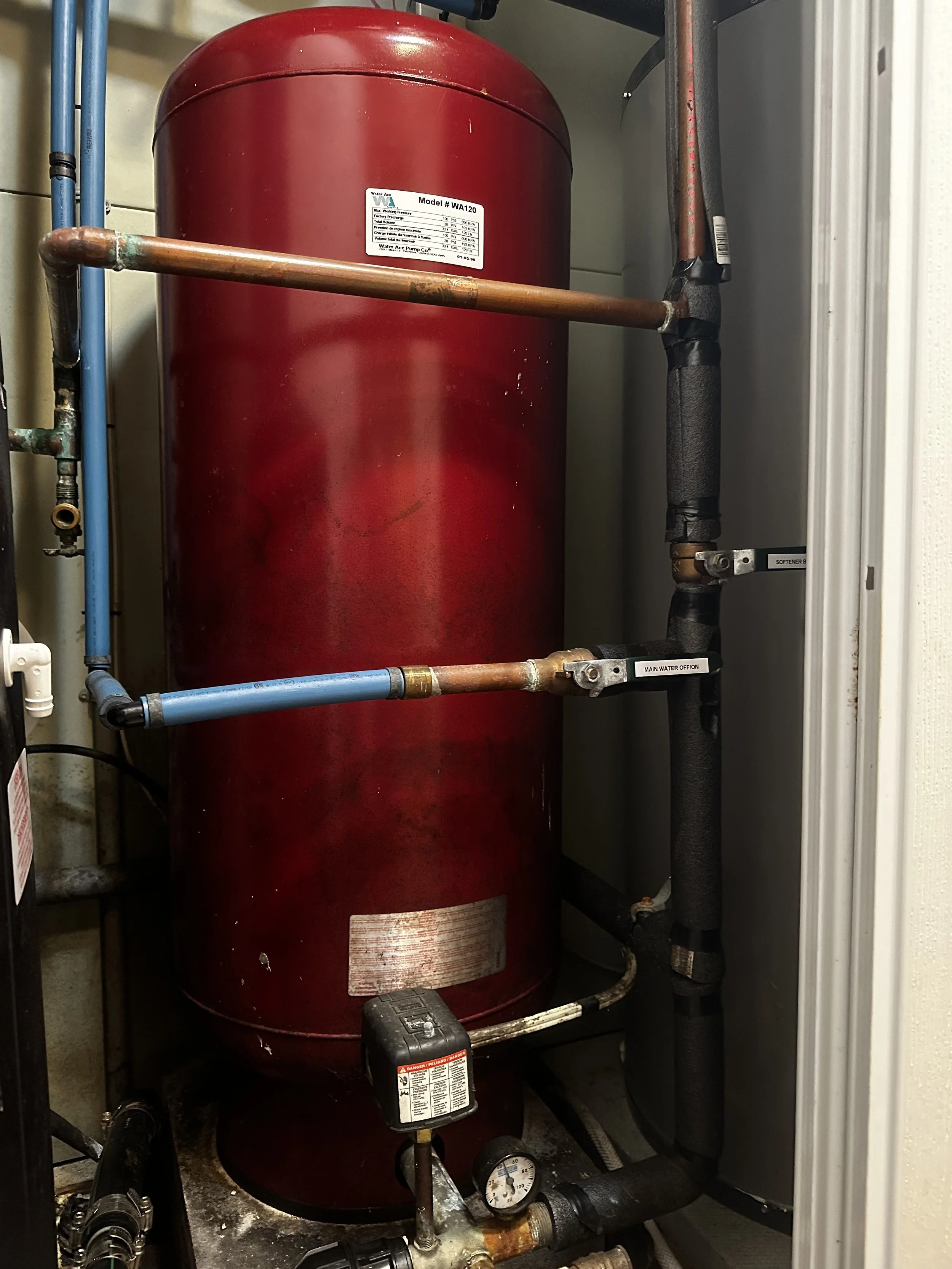Red water heater tank with pipes and control valves in a utility closet.