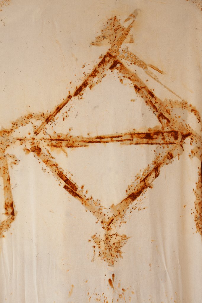 An abstract design created with some reddish-brown powder on a beige surface, forming a diamond shape with lines and splatters.