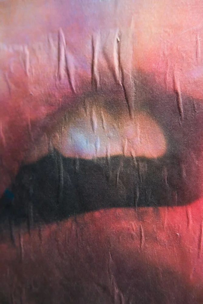 Close-up of a painted face with lips and nose with a textured surface and rainbow-colored hues.