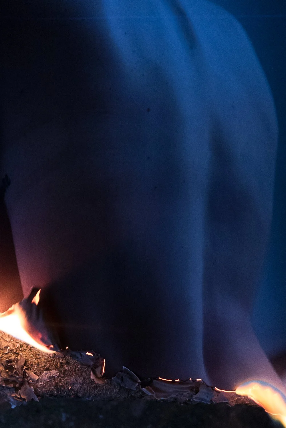 Close-up of a dark blue fabric with flames burning at the bottom edge.