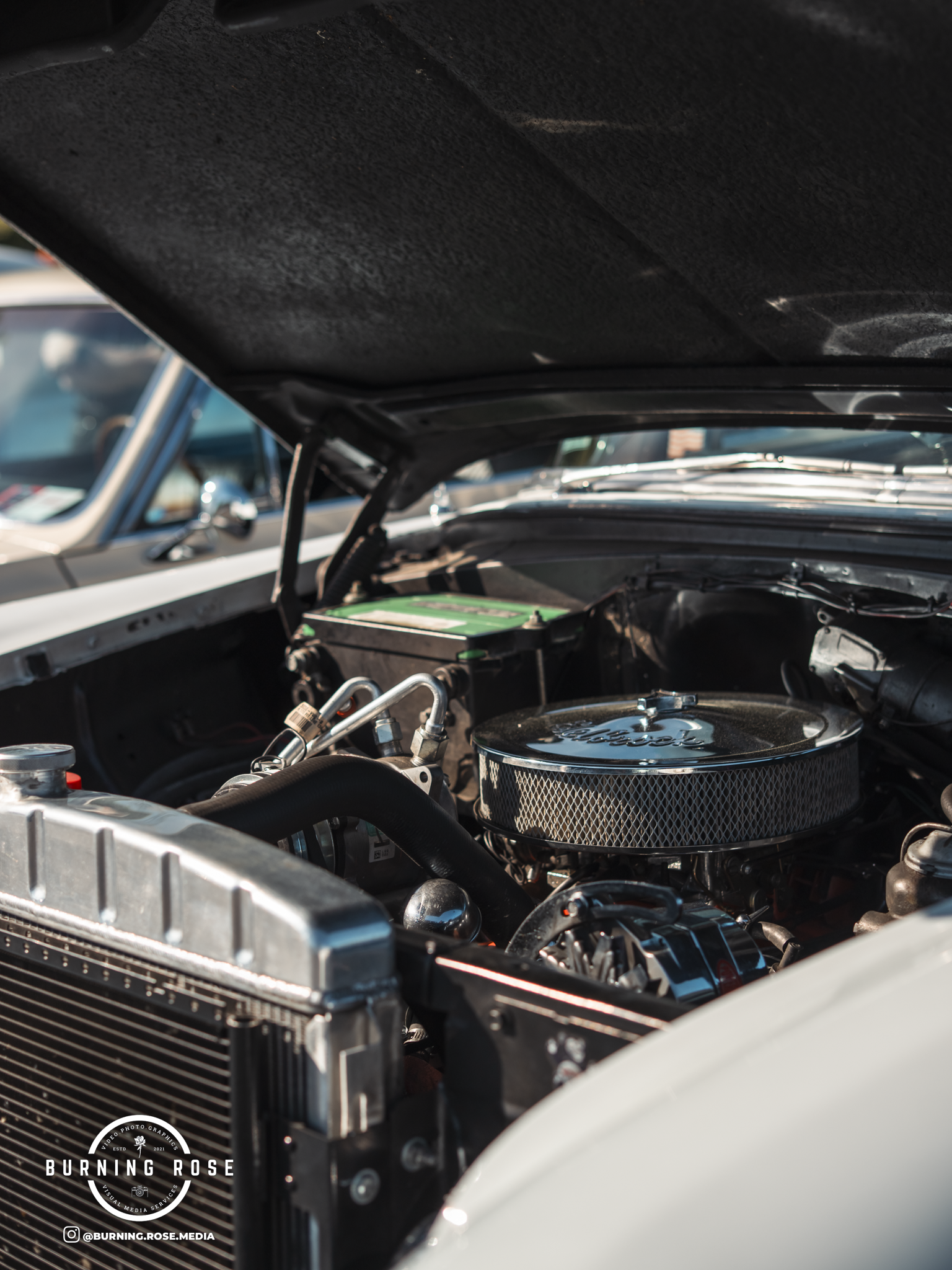 Close-up of the engine bay of a classic car, showing the radiator, engine components, and a round air filter with a logo.