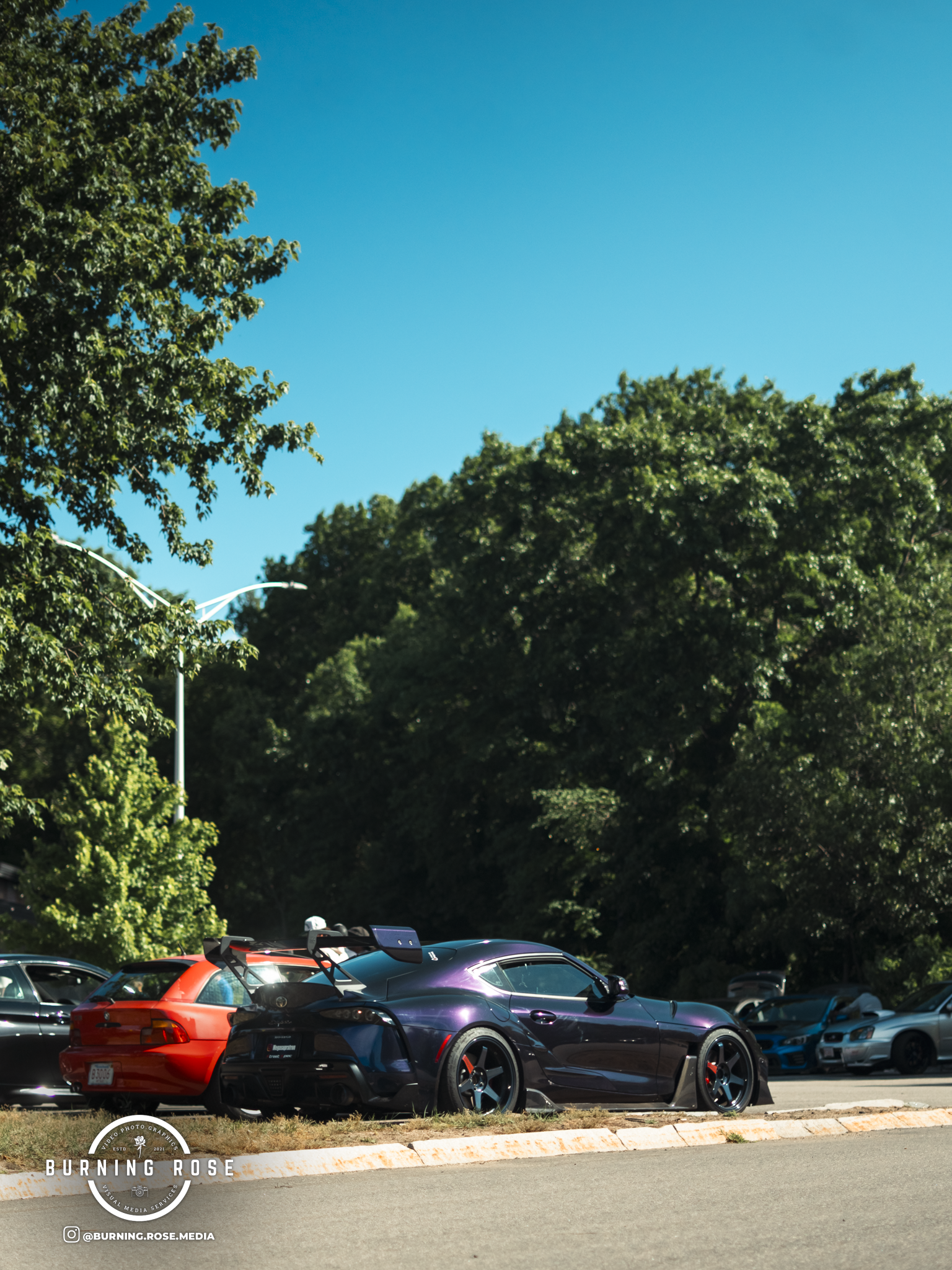 A parking lot filled with cars under a clear blue sky with green trees in the background.