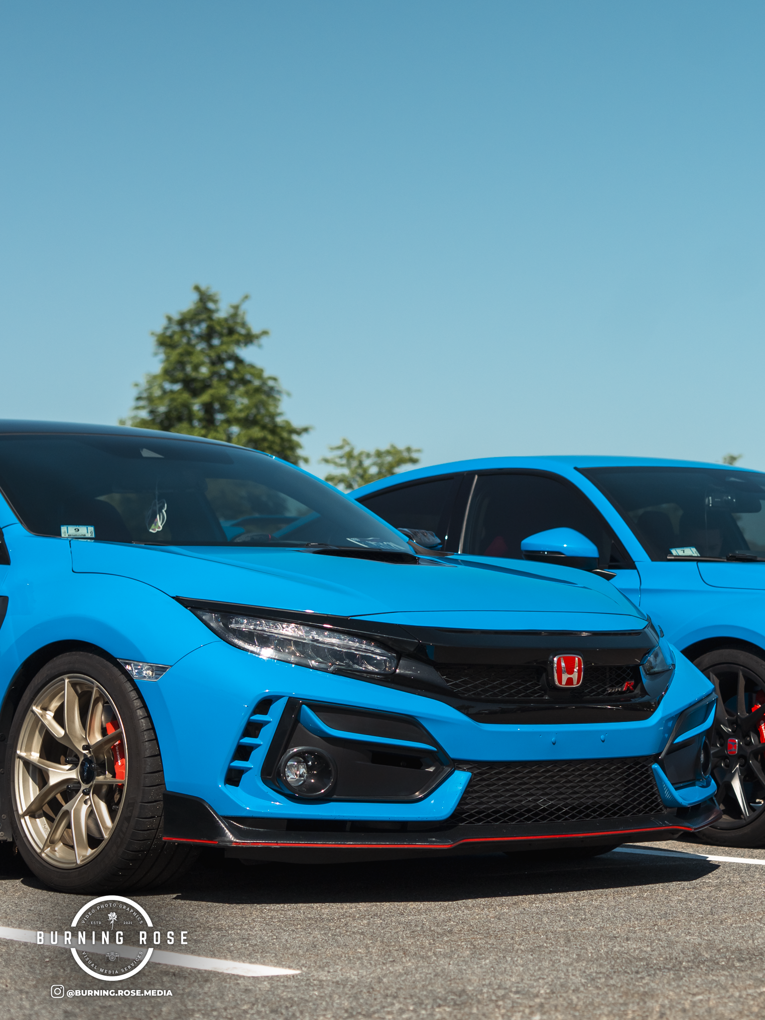 Blue Honda Civic Type R parked in a lot with trees and a clear blue sky in the background.