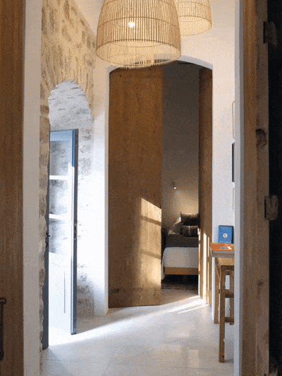 Entrance hallway with hanging wicker light fixtures, a stone wall on the left, an open doorway leading to a bedroom, and a small table with a book and a decorative object on it.