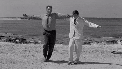 Two men walking on a beach with their arms outstretched.